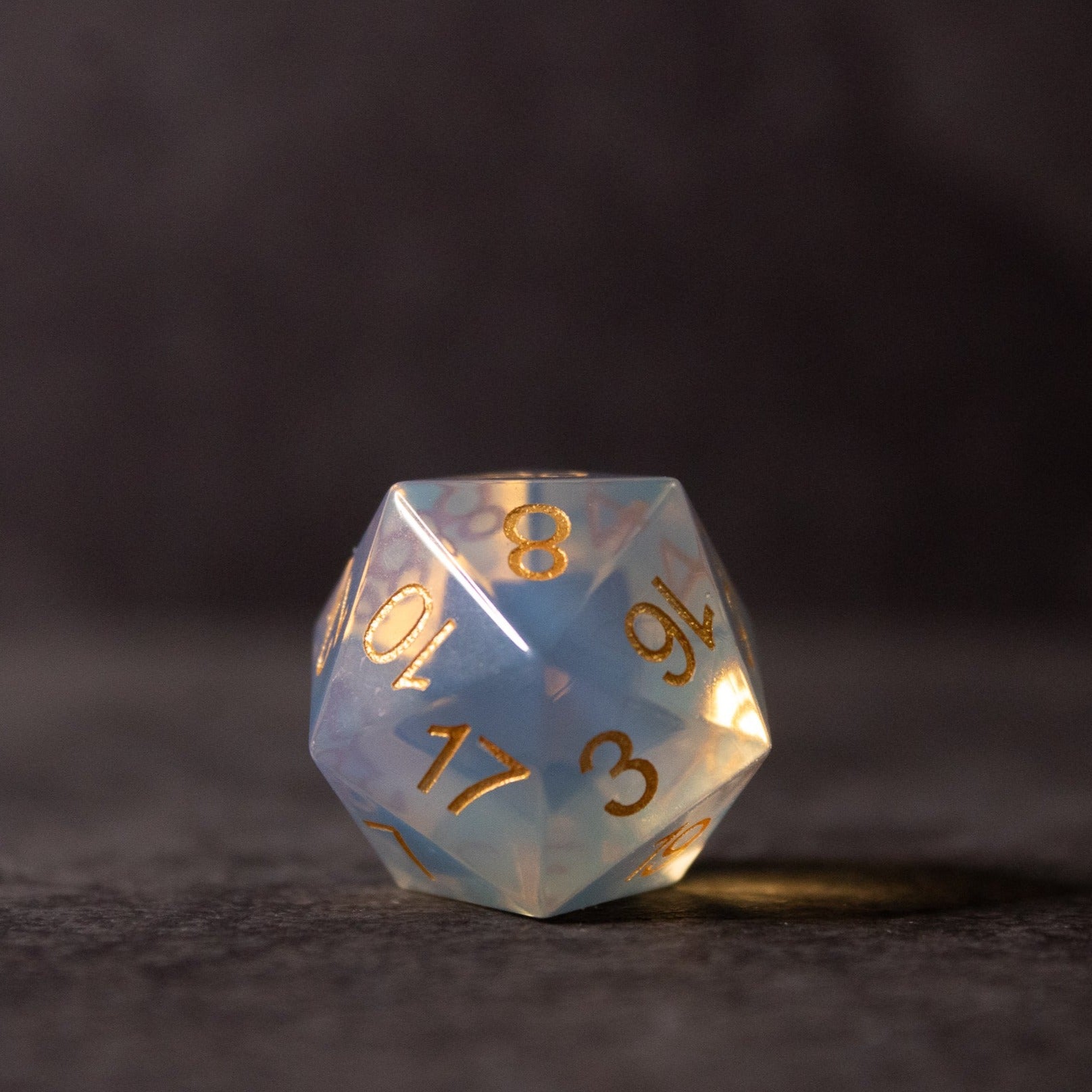 Opalite Gemstone Dice Set - Translucent opalite d20 gemstone die with gold numbering, glowing blue and white hues.