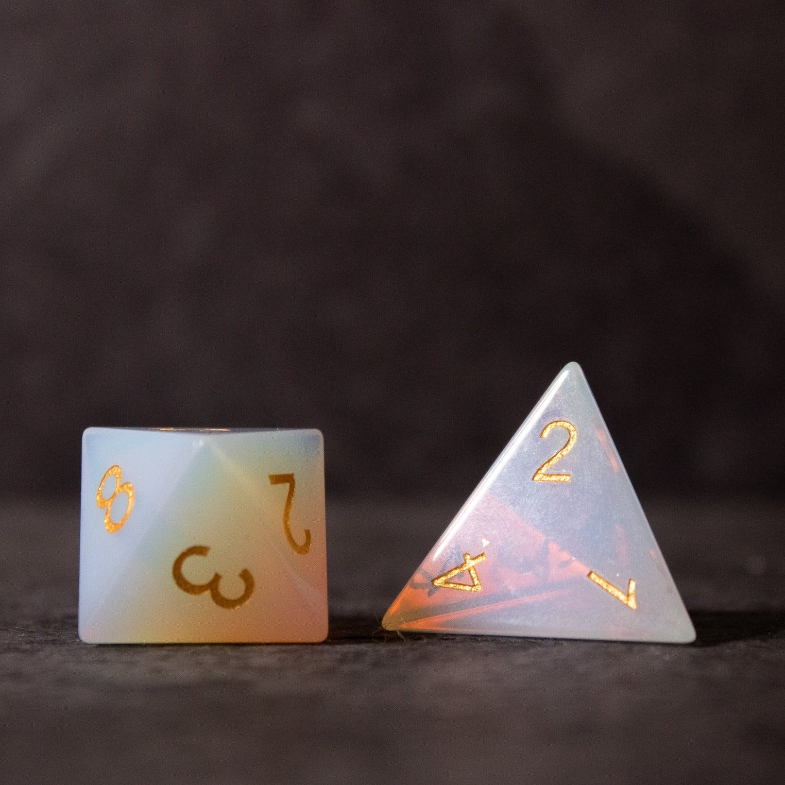 Opalite Gemstone Dice Set - Translucent opalite d20 and d4 gemstone dice with gold engraved numbers on dark background.