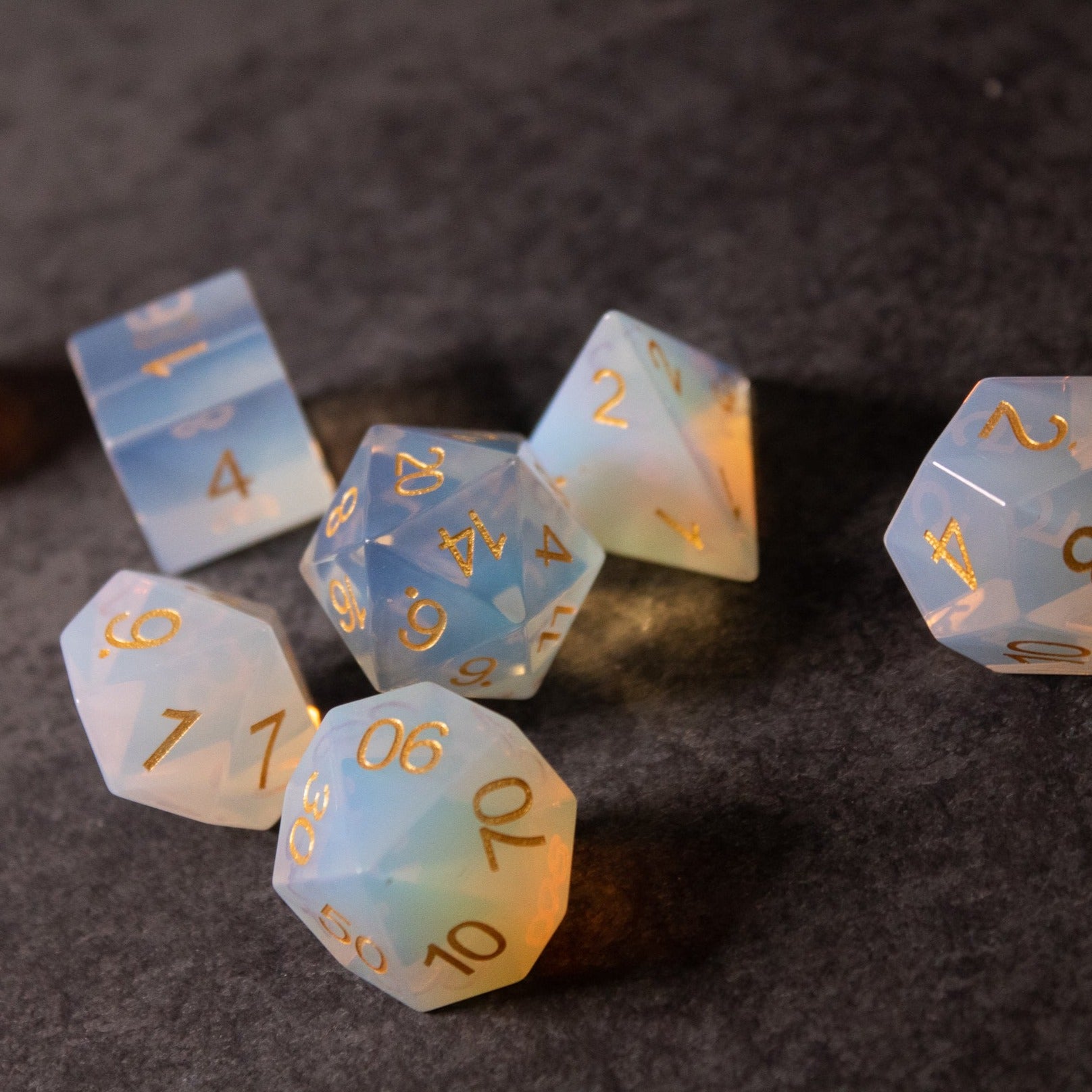 Opalite Gemstone Dice Set - Translucent opalite gemstone dice set with iridescent blue and white hues, gold numbering, various polyhedral shapes.