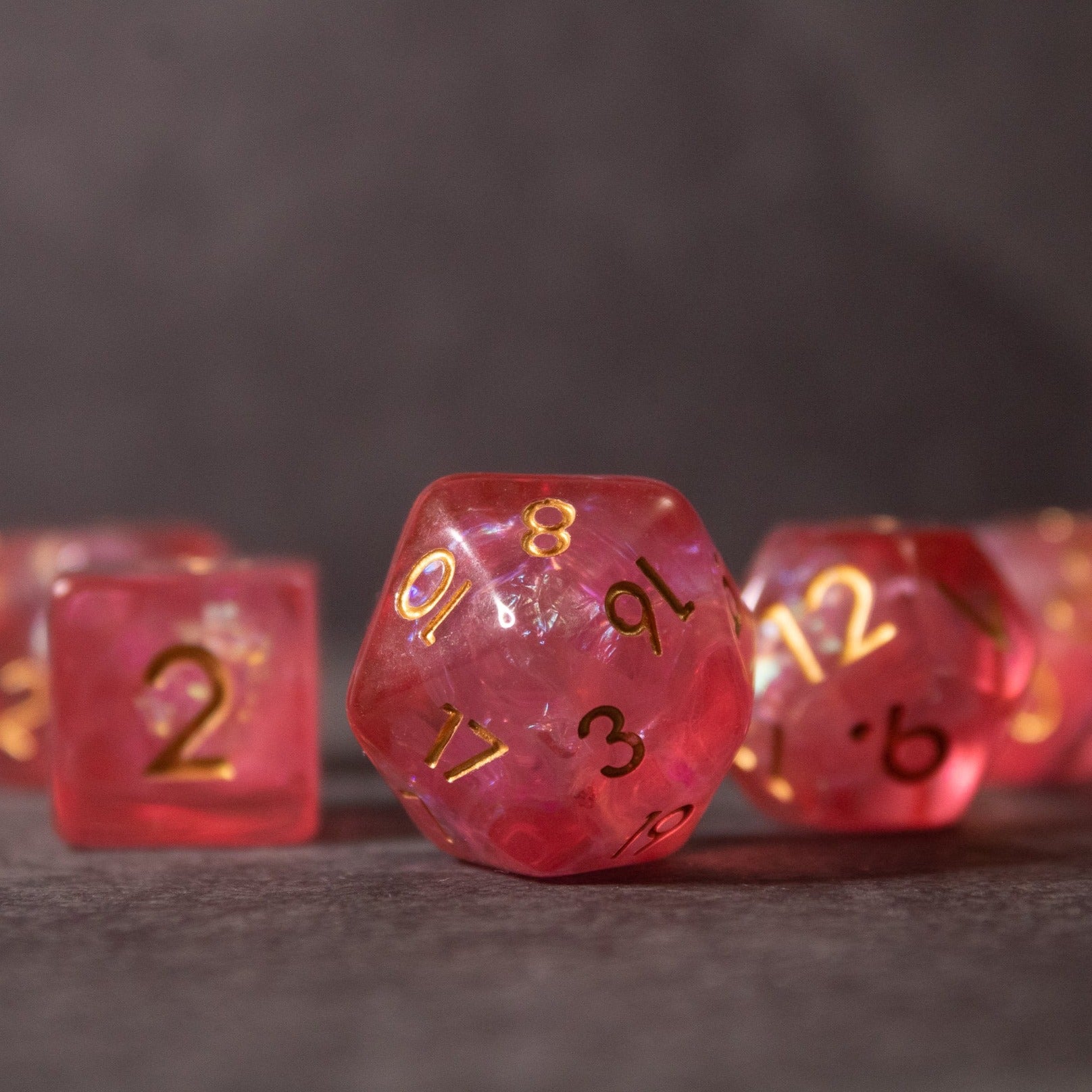 Pink Iridescent Dice Set - Pink iridescent polyhedral dice set with gold numbering on a dark surface.