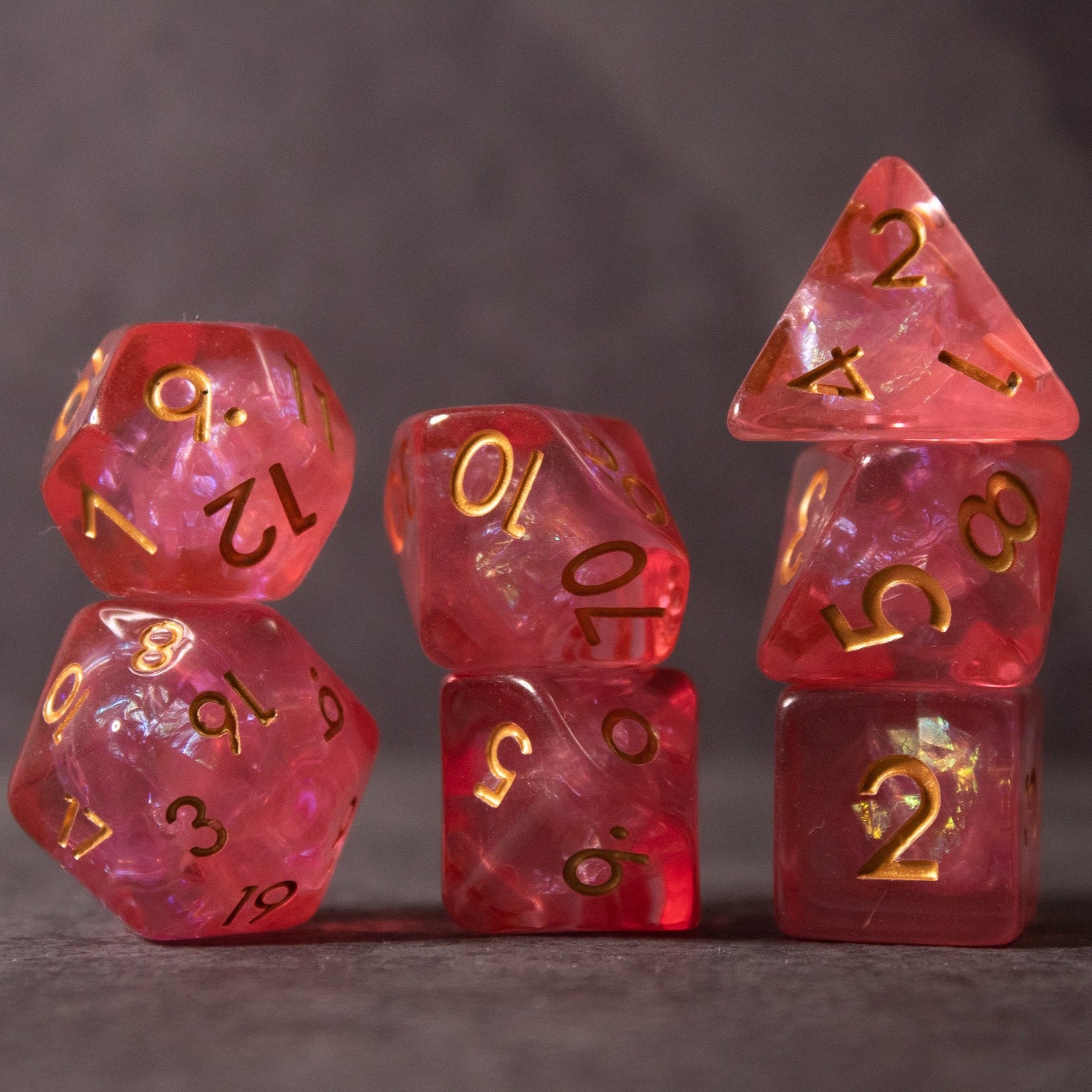 Pink Iridescent Dice Set - Set of seven pink iridescent standard gaming dice with gold numbers on a dark surface.