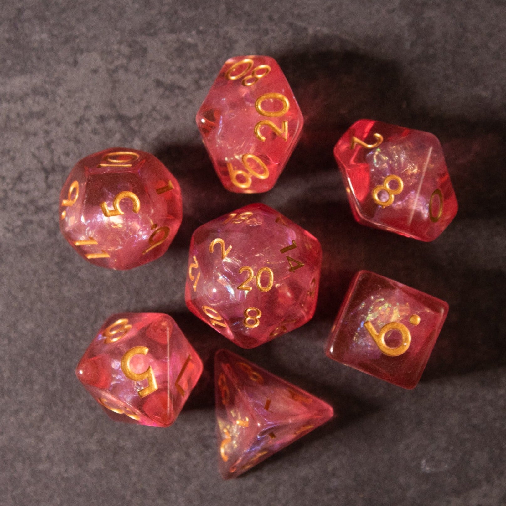 Pink Iridescent Dice Set - Seven pink iridescent polyhedral dice with gold numbers, including d20, d12, d10, d8, d6, and d4.