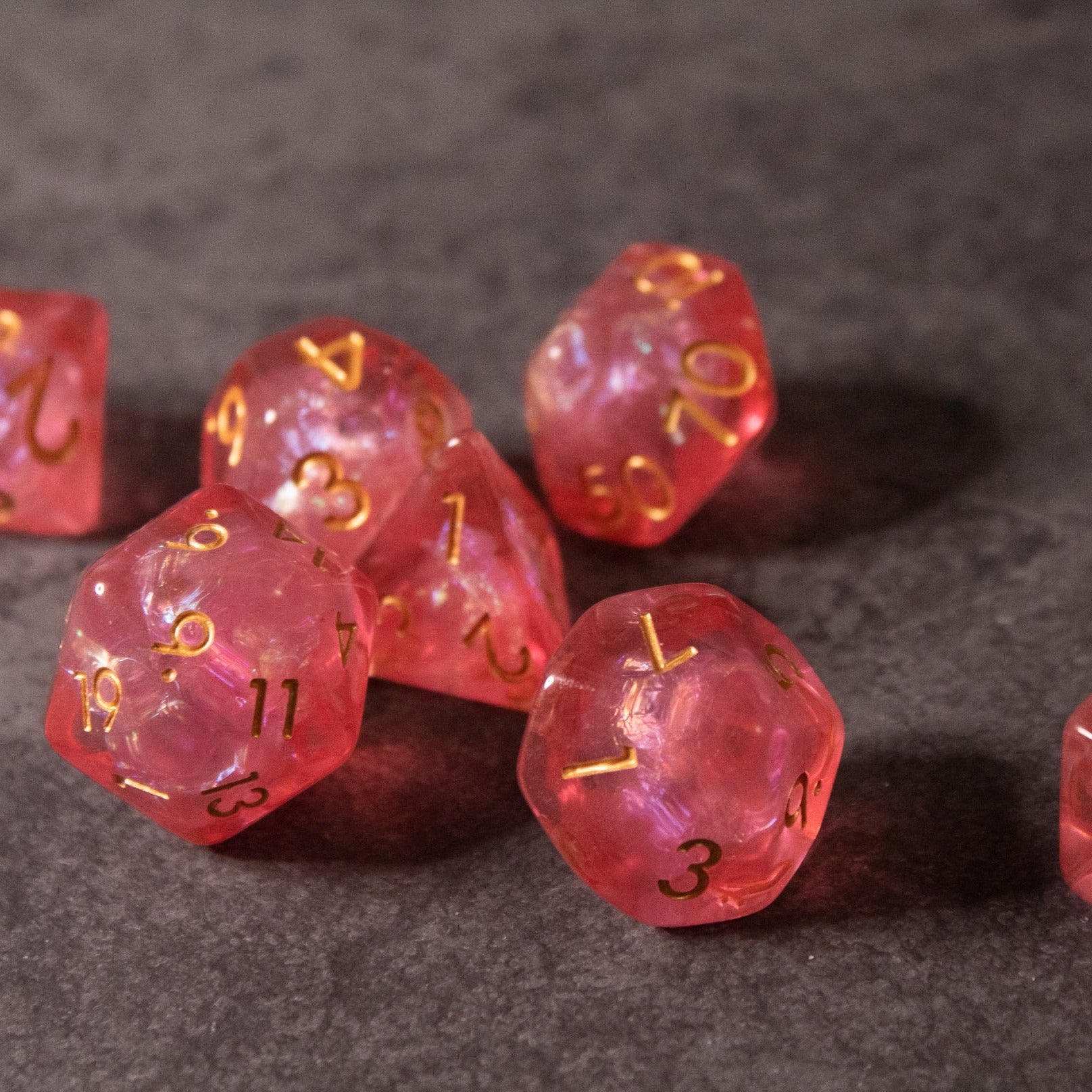 Pink Iridescent Dice Set - Pink translucent polyhedral dice set with gold numbers, including d20 and d12 shapes.