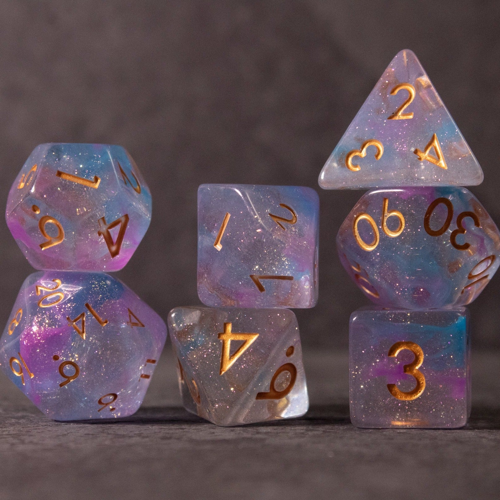 Cotton Candy Dice Set - Set of translucent dice in pink and blue shades with gold numbers, featuring standard polyhedral shapes.