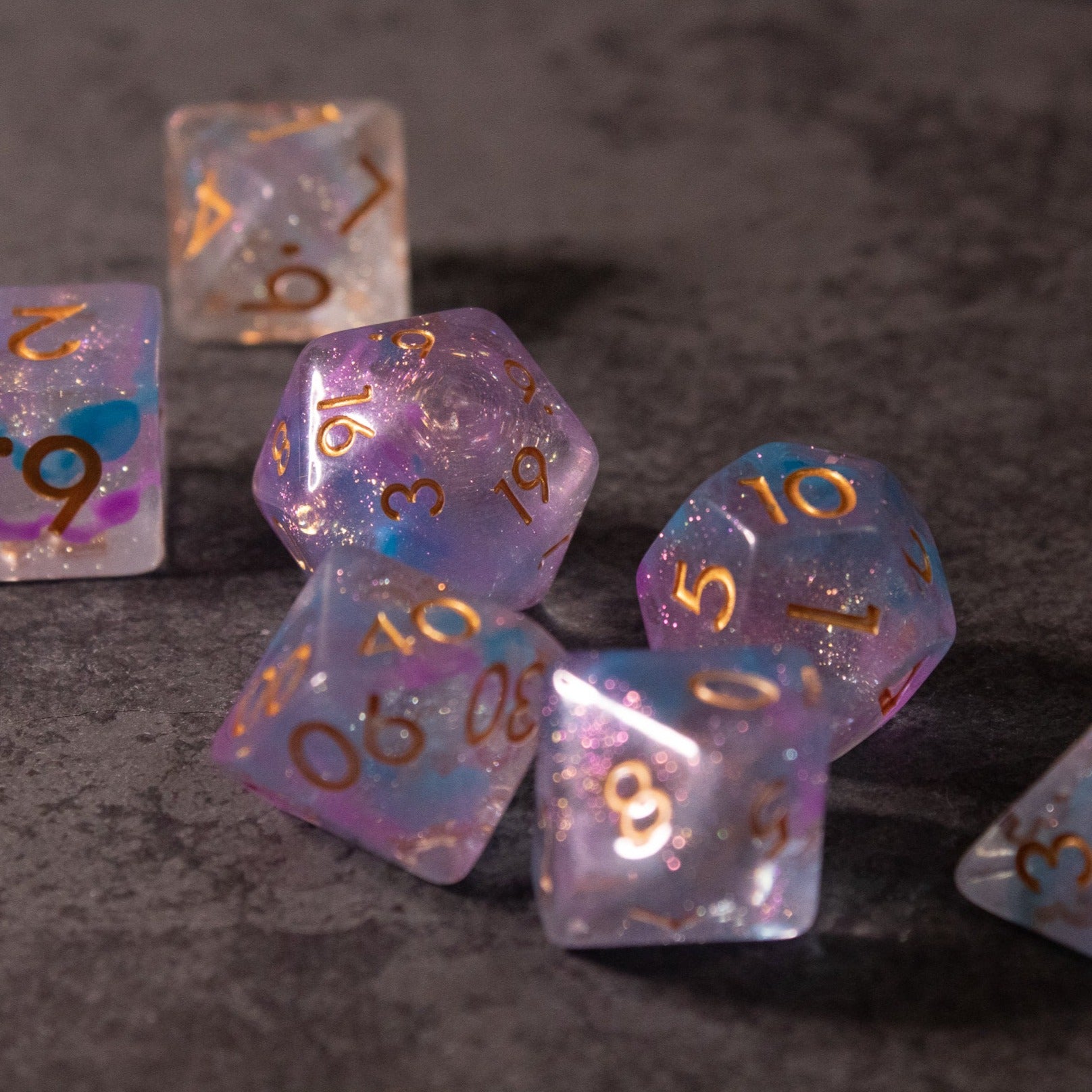 Cotton Candy Dice Set - Translucent pink and blue polyhedral dice set with gold numbers on a dark surface.