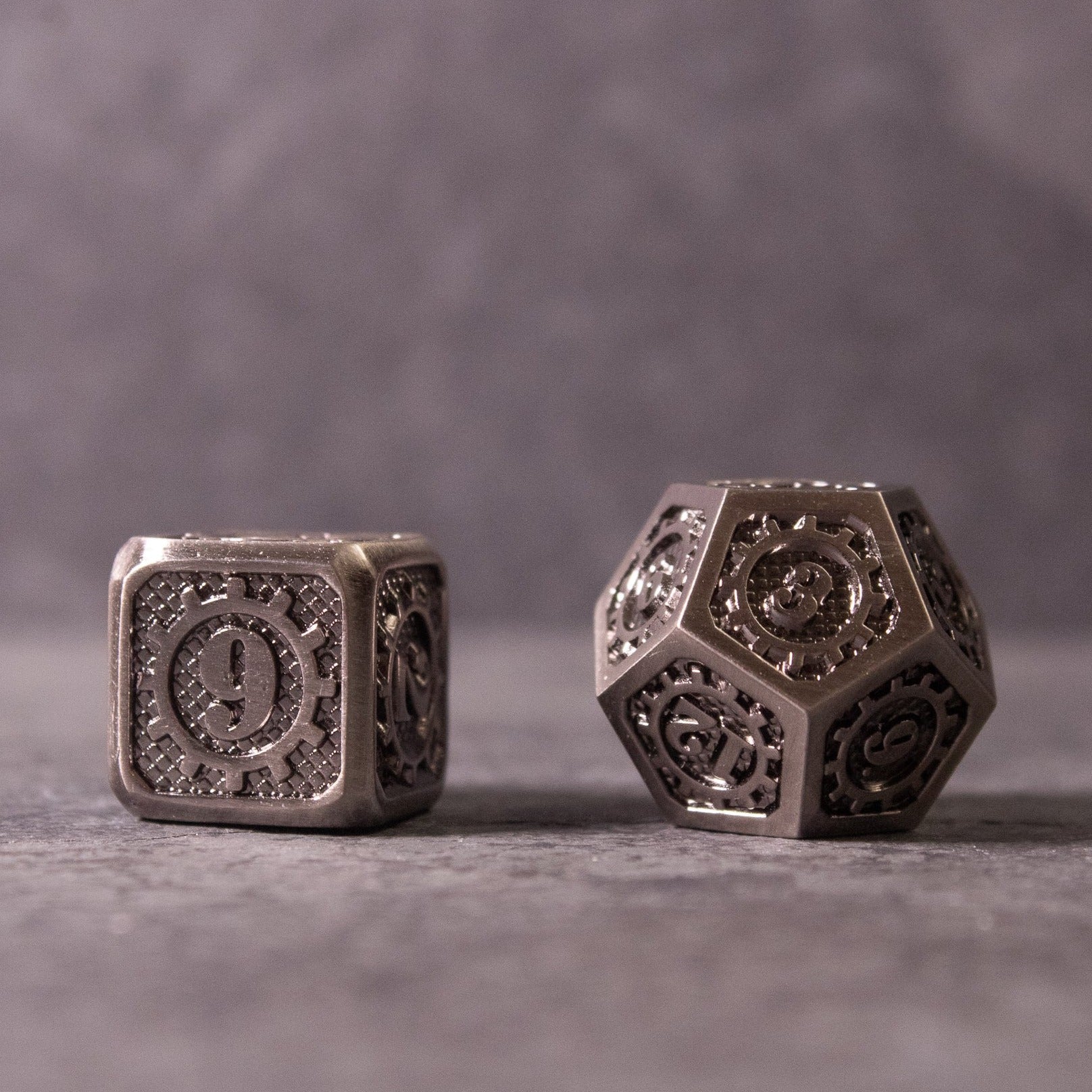 Metal Gear Dice Set - Metal gear-themed metal d20 and d6 dice with intricate cogwheel design on gray surface.