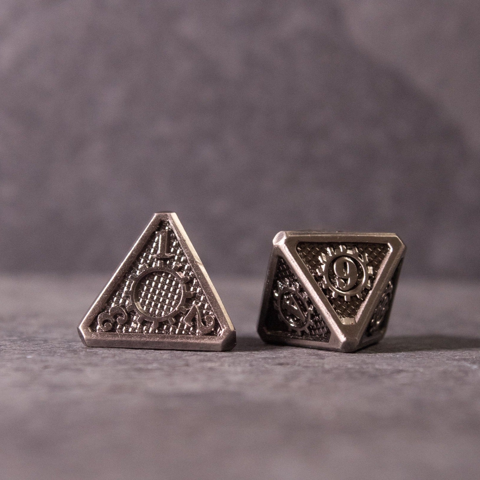 Metal Gear Dice Set - Two silver metal four-sided dice with intricate gear and cog designs on each face, set against a neutral gray background.