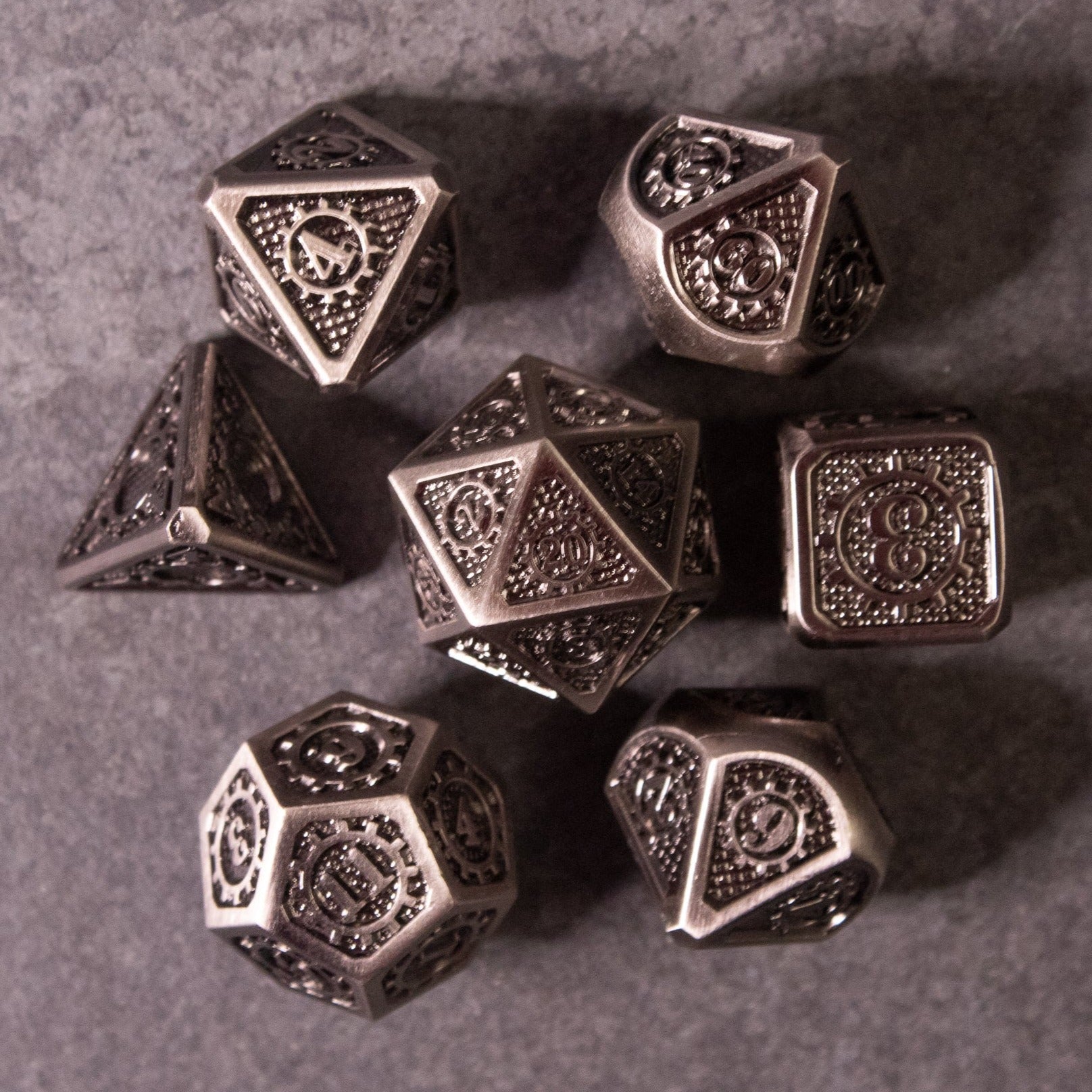 Metal Gear Dice Set - Set of seven metallic polyhedral dice with intricate gear and cog designs engraved on each face, finished in dark.