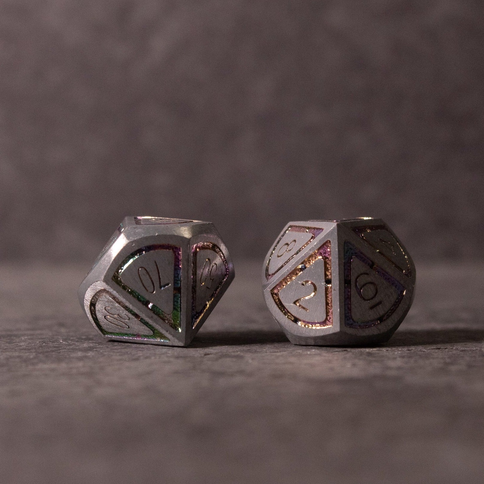 Prismatic Core Dice Set - Two metal polyhedral dice with prismatic, reflective surfaces and engraved numbers, showing a d20 shape.