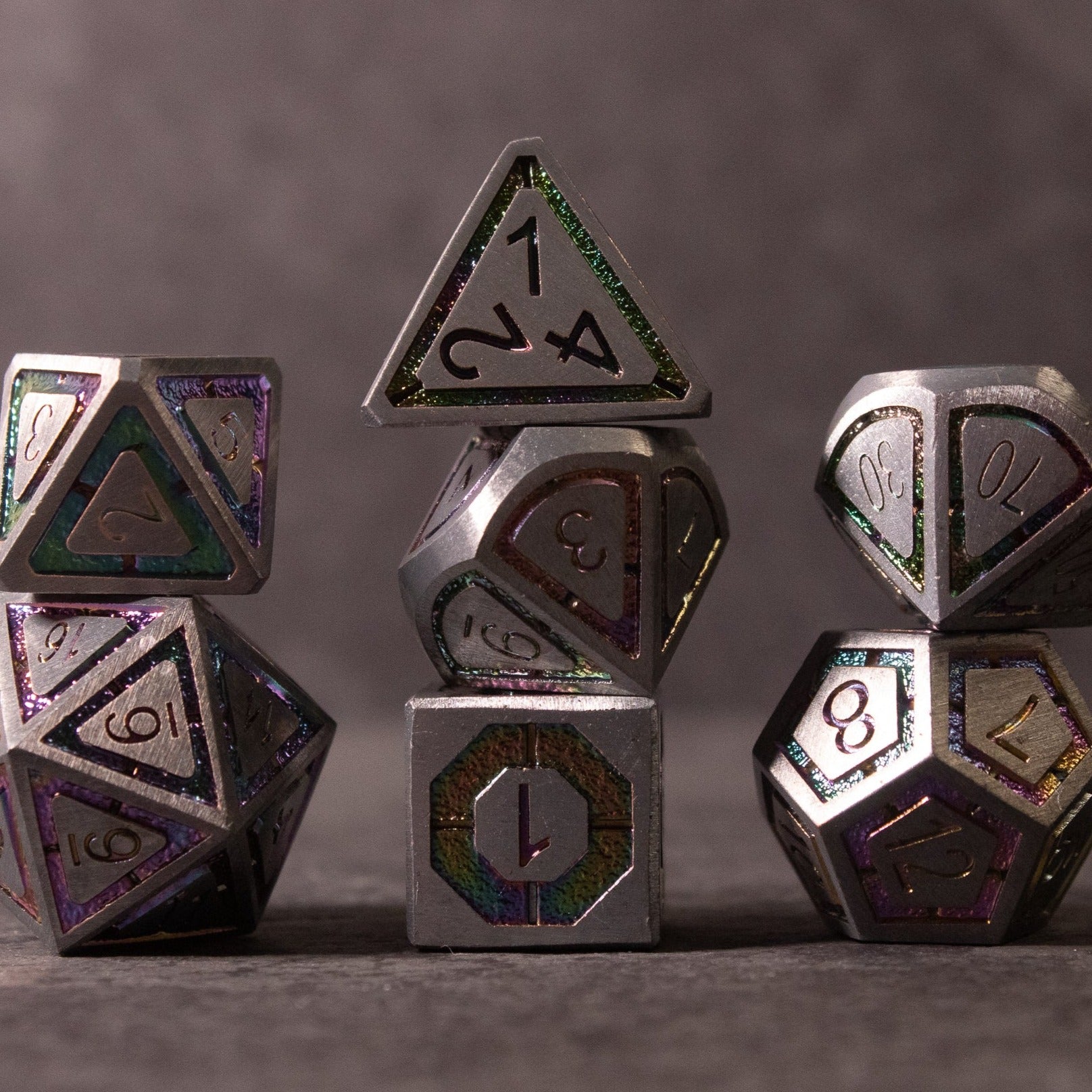 Prismatic Core Dice Set - Set of silver metal polyhedral dice with prismatic edges and engraved numbers on a dark background.