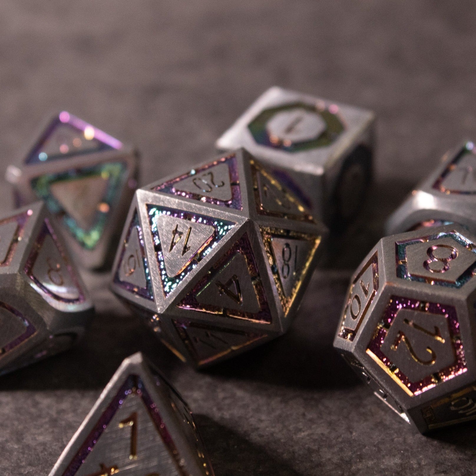 Prismatic Core Dice Set - Set of metallic polyhedral dice with a dark prismatic finish and engraved numbers filled with purple glitter accents.