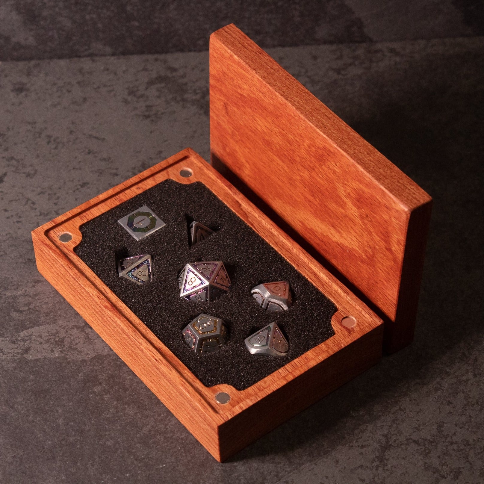 Prismatic Core Dice Set - Metallic black seven-piece polyhedral dice set with colorful prismatic numbers in an open wooden display box.