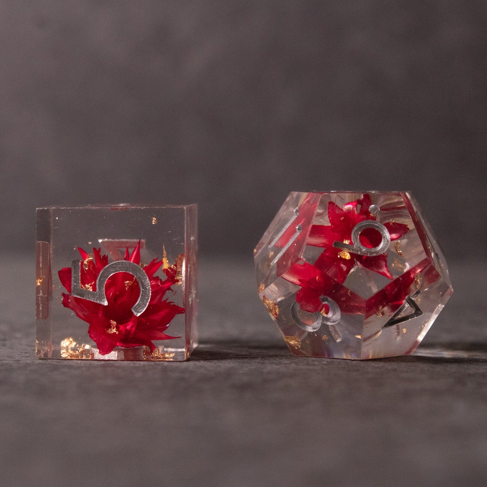Red Lotus Flower Dice Set - Clear sharp-edged dice with red lotus flower designs encased inside transparent resin, one cube and one d20 shape.