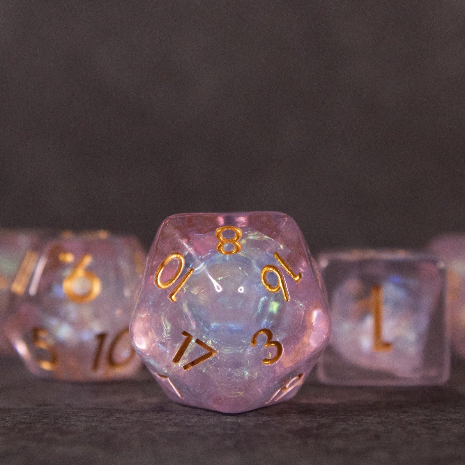 Sakura Dice Set - Iridescent pink twenty-sided die with gold numbers from Sakura Dice Set on dark background.