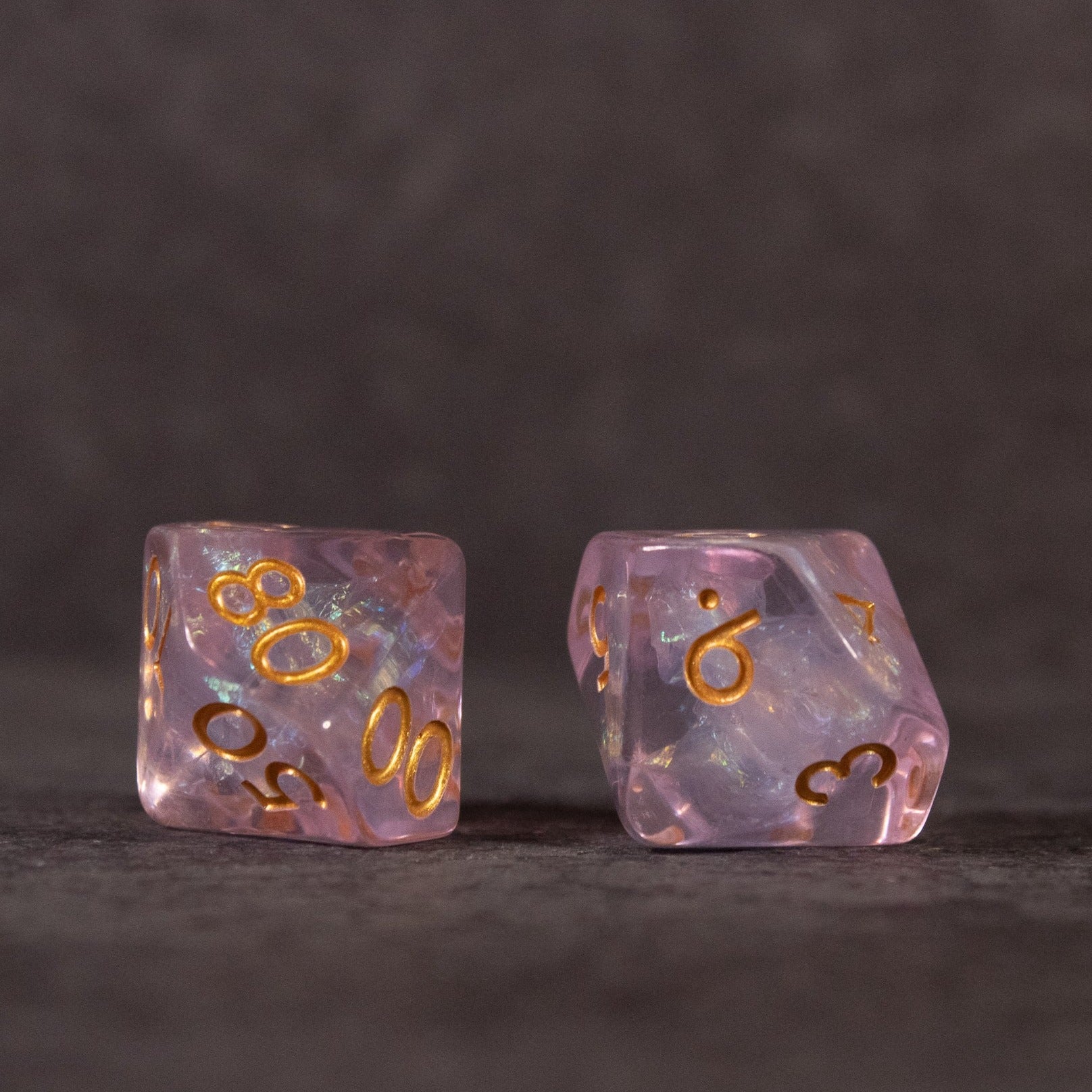 Sakura Dice Set - Two iridescent pink polyhedral dice with gold numbers, one showing 8 and 6, the other 9 and 3.