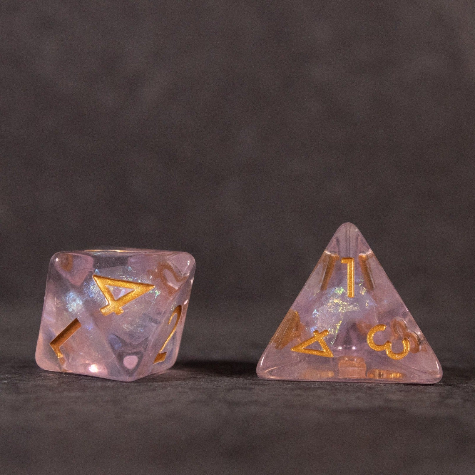 Sakura Dice Set - Iridescent pink polyhedral dice with gold numbers and embedded flower petal inclusions, shown are a d12 and a d4.