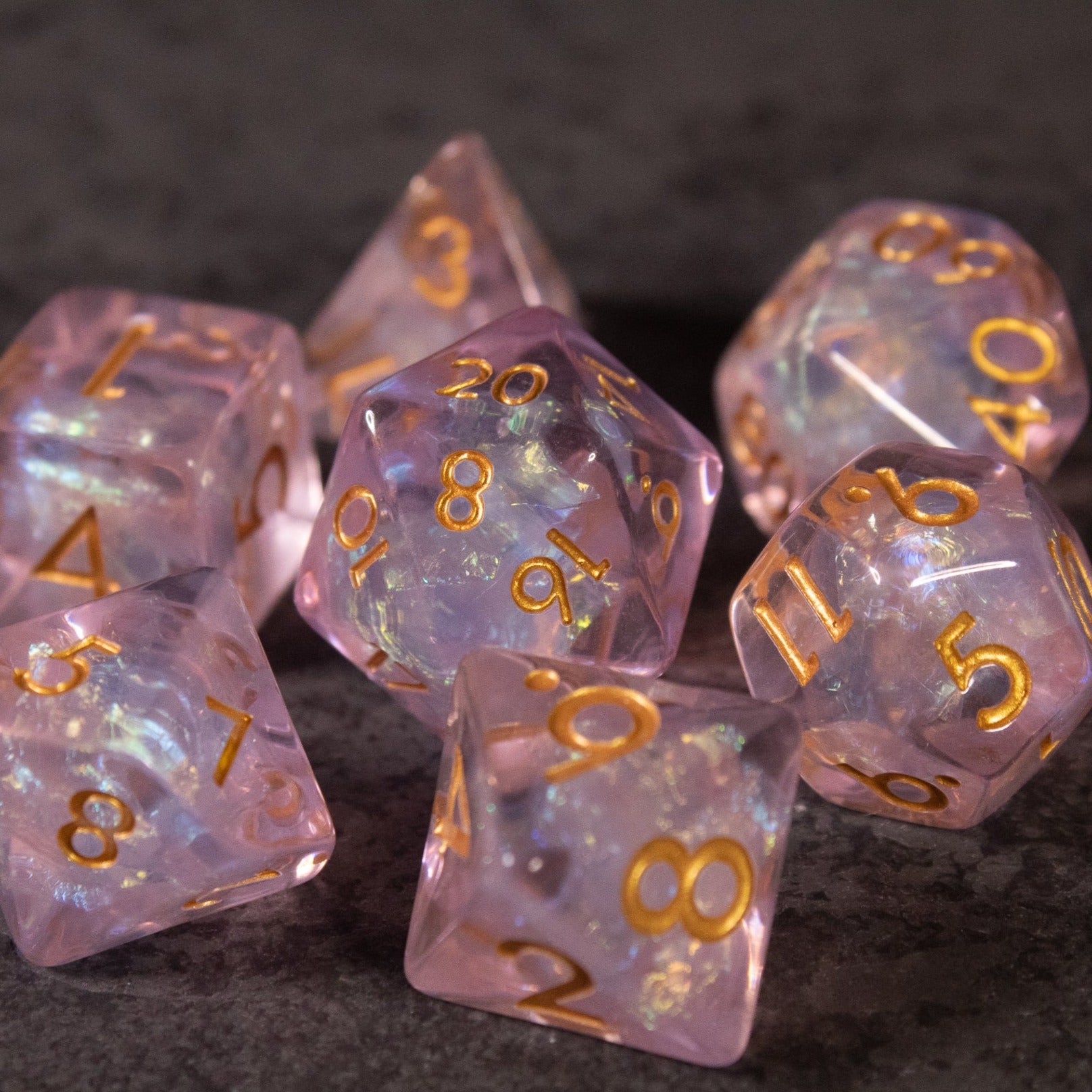 Sakura Dice Set - Iridescent pink polyhedral dice set with gold numbers, including d20, d12, d10, d8, d6, and d4.