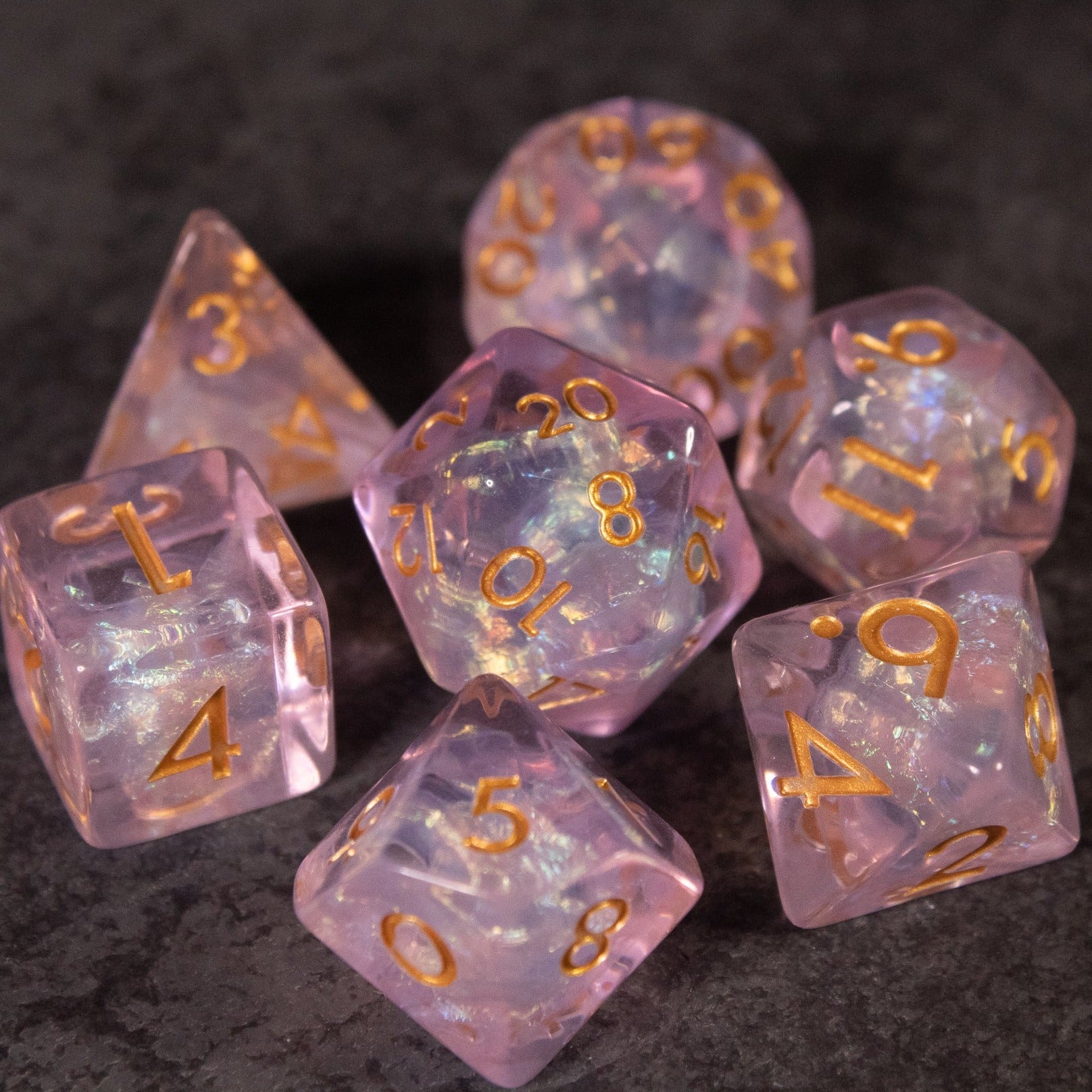 Sakura Dice Set - Set of seven iridescent pink polyhedral dice with gold numbers including d4, d6, d8, d10, percentile, d12, and d20.