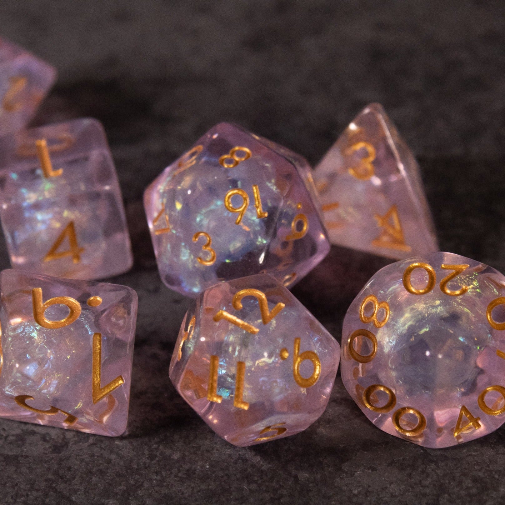 Sakura Dice Set - Iridescent pink polyhedral dice set with gold numbering, featuring translucent surfaces and shimmering inclusions.