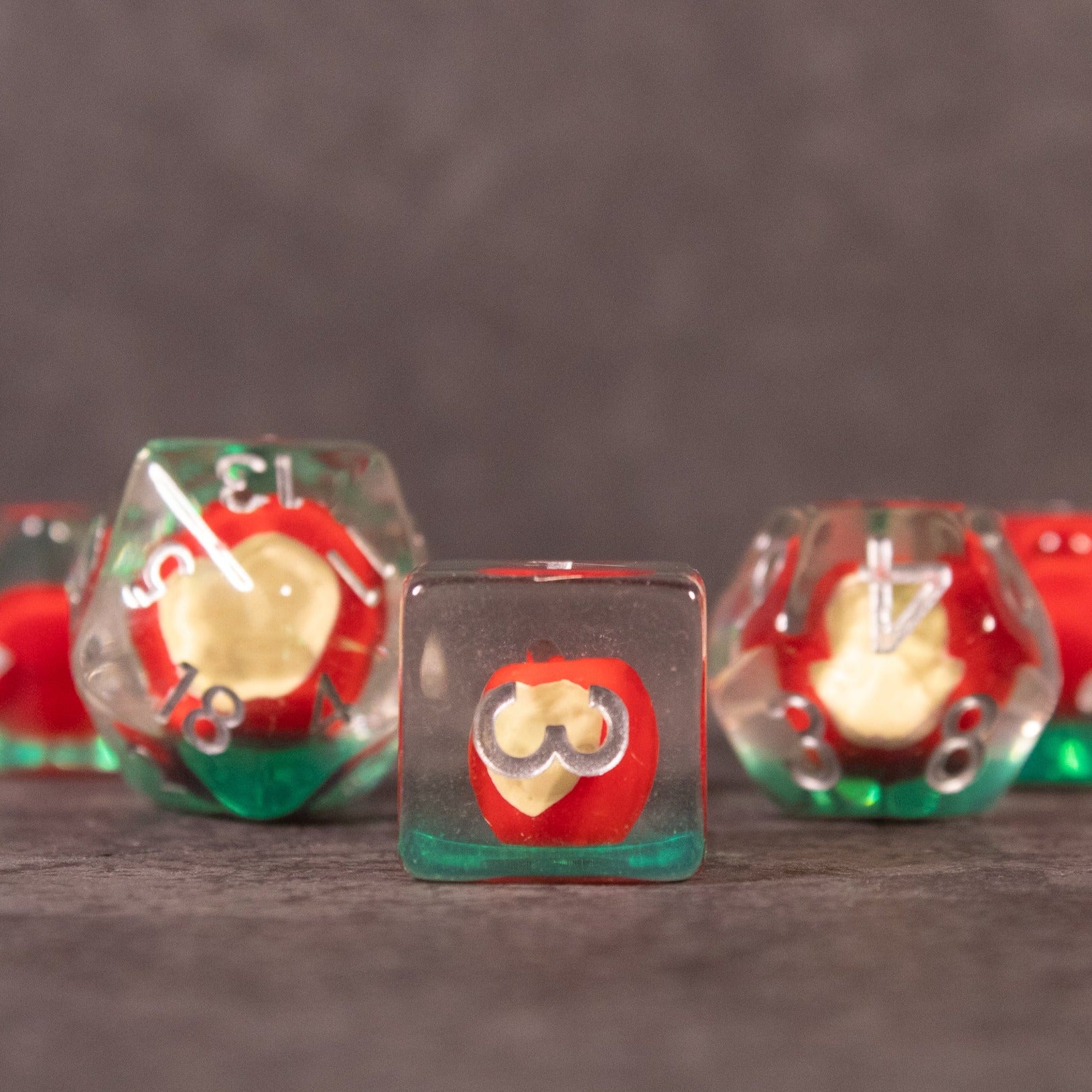 A set of polyhedral dice with a small, bitten apple design inside, featuring red and green translucent colors with white numbering.