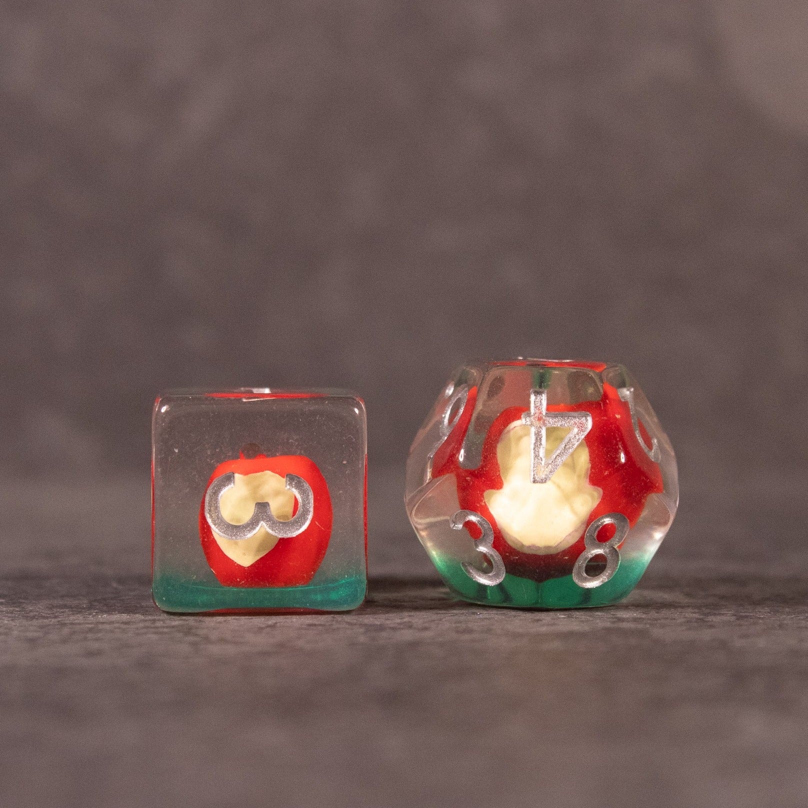 Apple Bite Dice Set - Clear resin dice with a red apple and bite detail inside, featuring white numbers on one die and an apple core on the other.