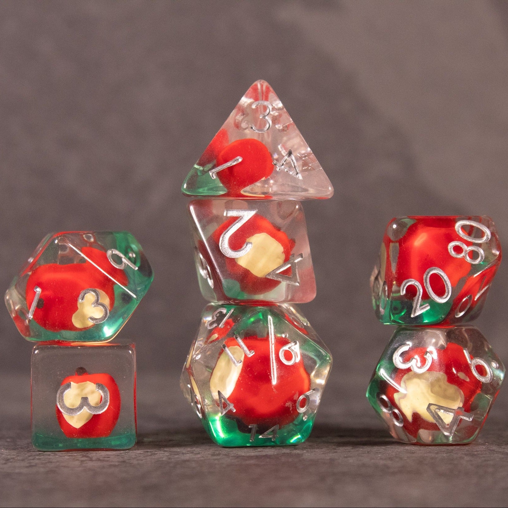 Apple Bite Dice Set - Set of transparent polyhedral dice with red apple core inclusions and white numbering.