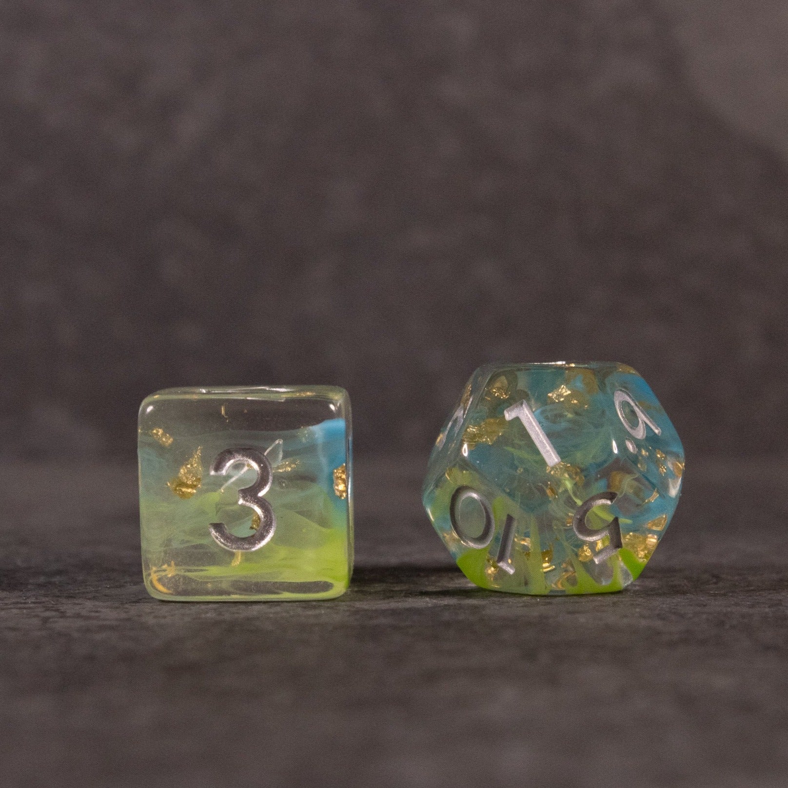Blue, Green, and Gold Swirl Dice Set - Blue, green, and gold swirl dice set with clear base and silver numbers, showing a six-sided and a ten-sided die.