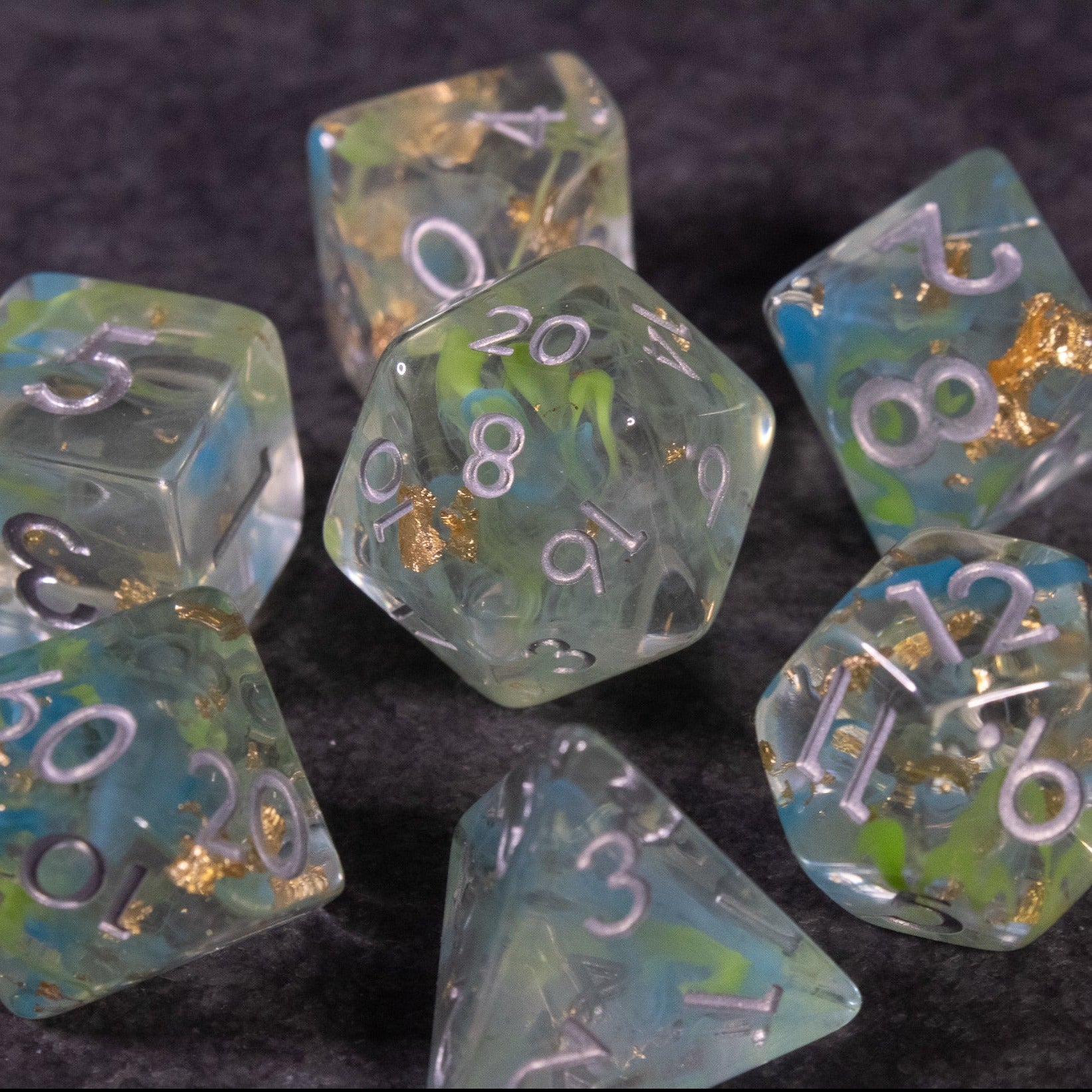 Blue, Green, and Gold Swirl Dice Set - Translucent dice set with blue, green, and gold swirls and white numbers on a dark background.