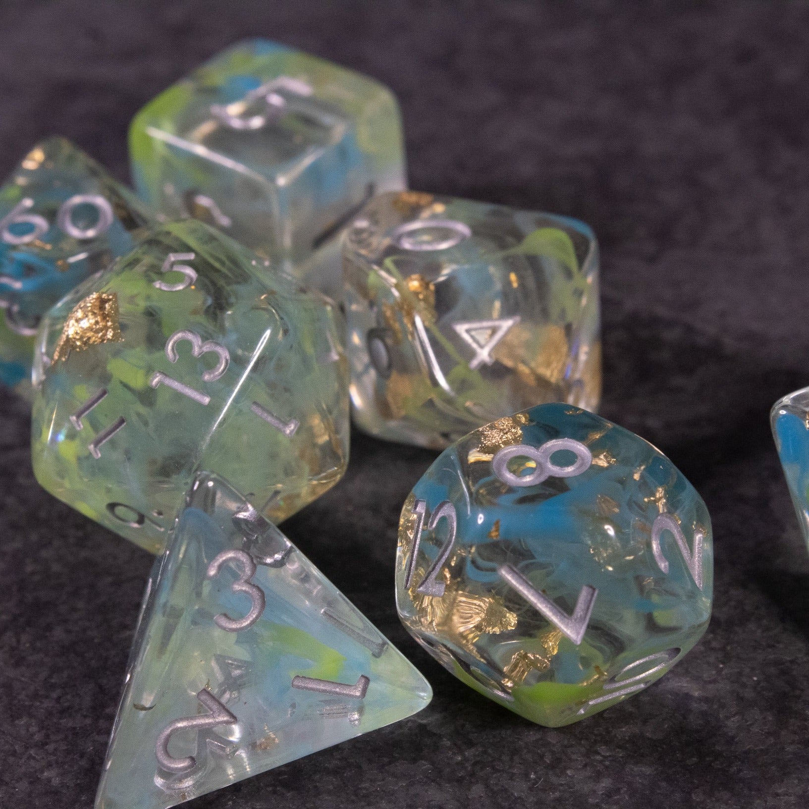 Blue, Green, and Gold Swirl Dice Set - Blue, green, and gold swirl polyhedral dice set with metallic numbers on a dark background.