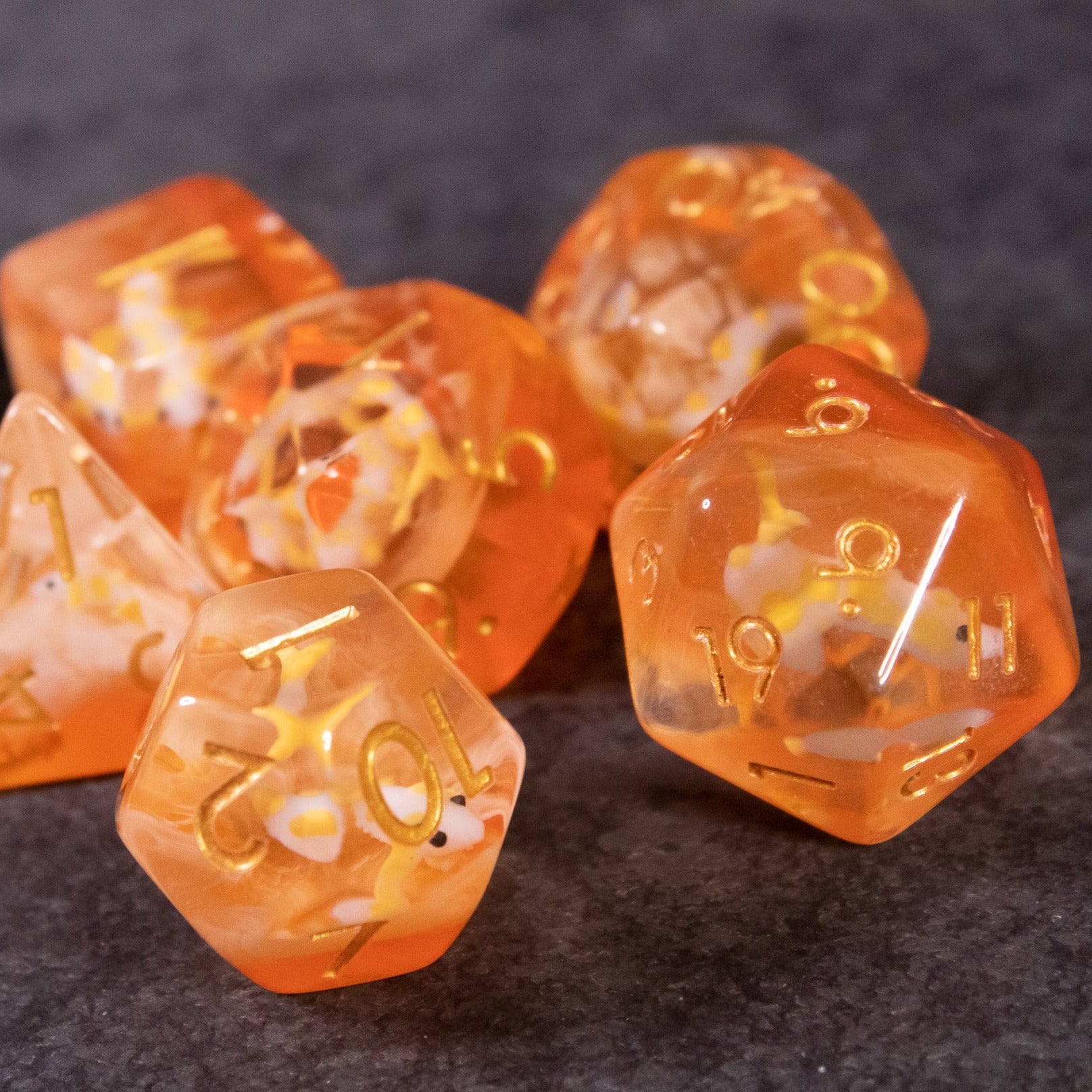 Orange Koi Fish Dice Set - Set of translucent orange polyhedral dice with gold numbers featuring koi fish inclusions.