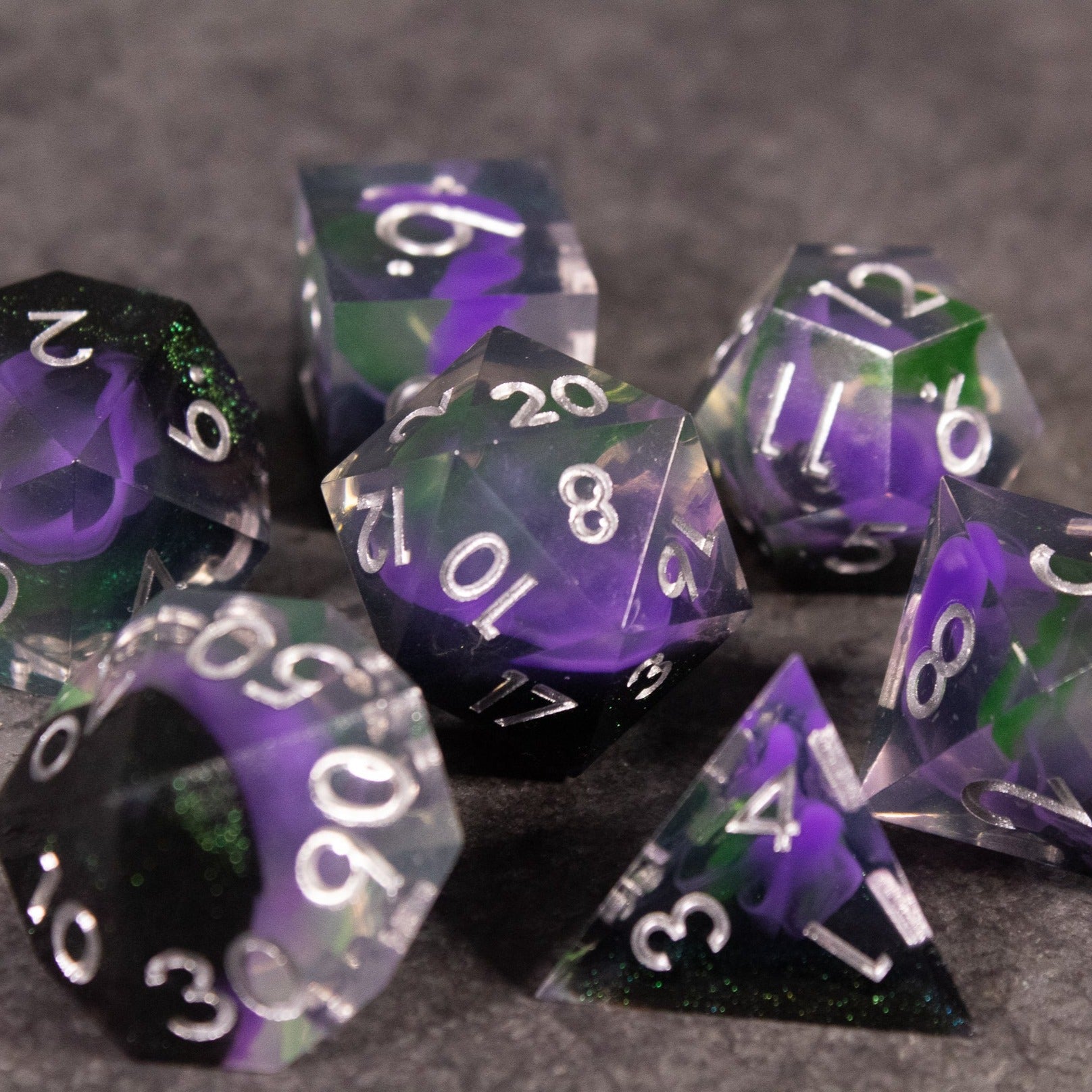 Witch's Brew Dice Set - Set of transparent sharp-edged polyhedral dice with swirling green and purple colors and white numbering.
