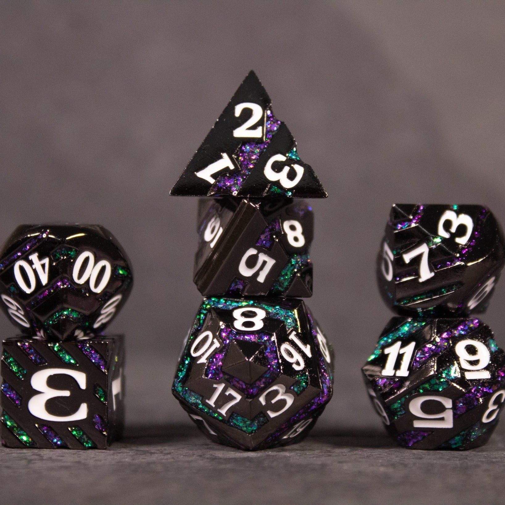 Arcane Leyline Dice Set - Purple & Green - Set of seven multifaceted metal dice in purple and green with white numbering, featuring various shapes including a d20,.