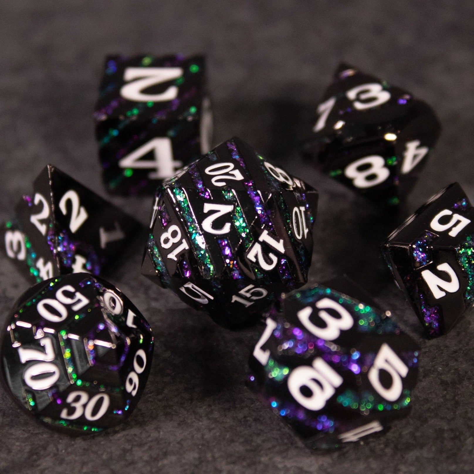Arcane Leyline Dice Set - Purple & Green - Seven dark polyhedral metal dice with purple and green reflective swirls and white numbering.