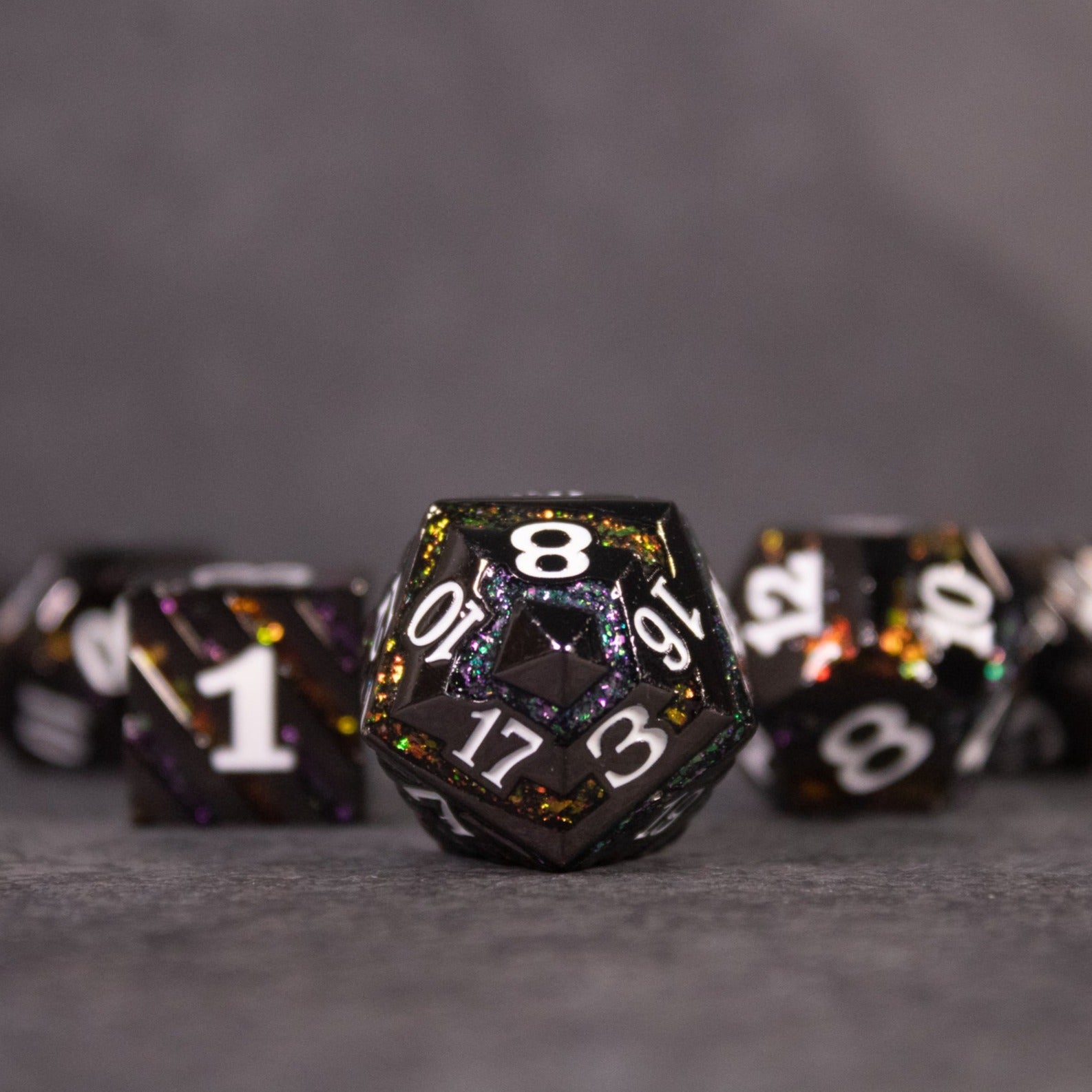 Arcane Leyline Dice Set - Orange & Pink - Black metal polyhedral dice with orange and pink iridescent flakes and white numbering, 20-sided die in focus.