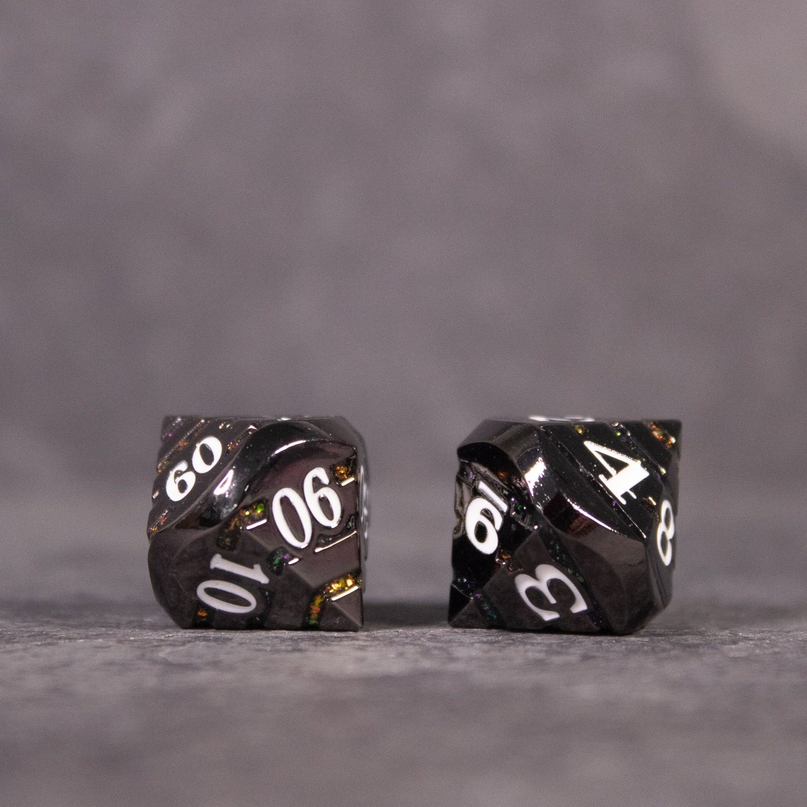 Arcane Leyline Dice Set - Orange & Pink - Two black metal polyhedral dice with white numbers and subtle orange and pink accents on a gray surface.