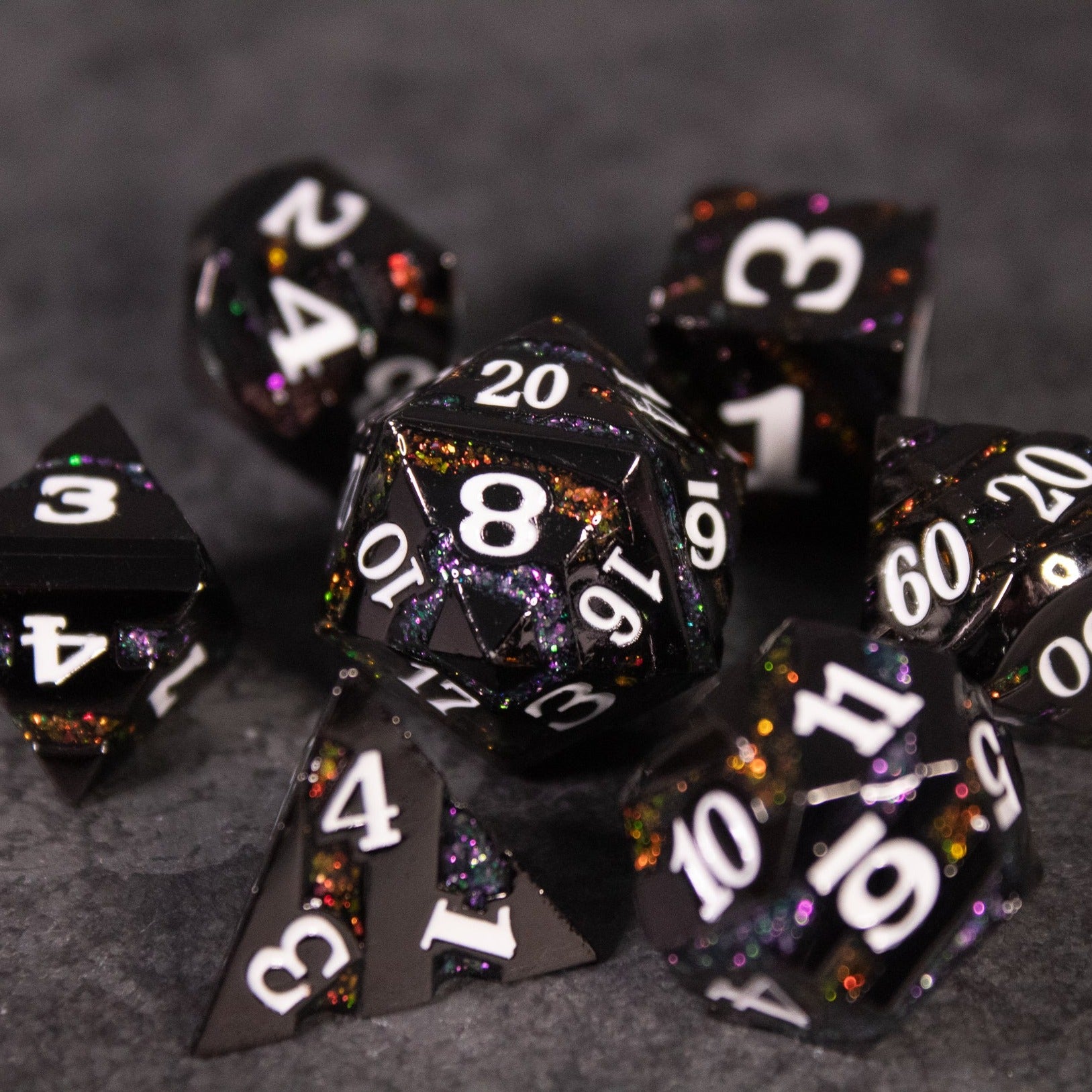 Arcane Leyline Dice Set - Orange & Pink - Set of seven black metal dice with orange and pink flecks and white numbering on dark gray background.
