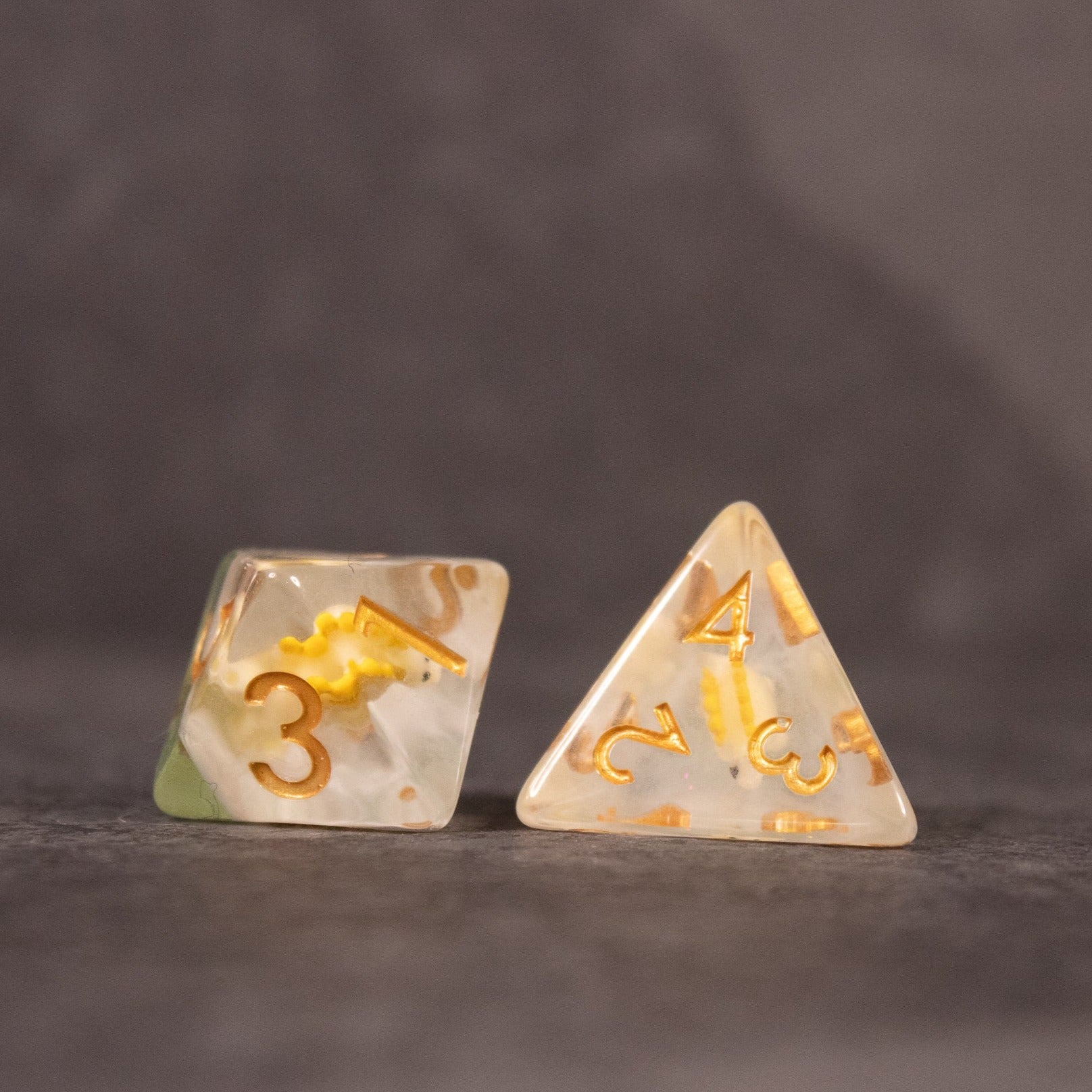 Yellow Stegosaurus Dice Set - Yellow translucent four-sided and six-sided dice with gold numbers and embedded stegosaurus figures.