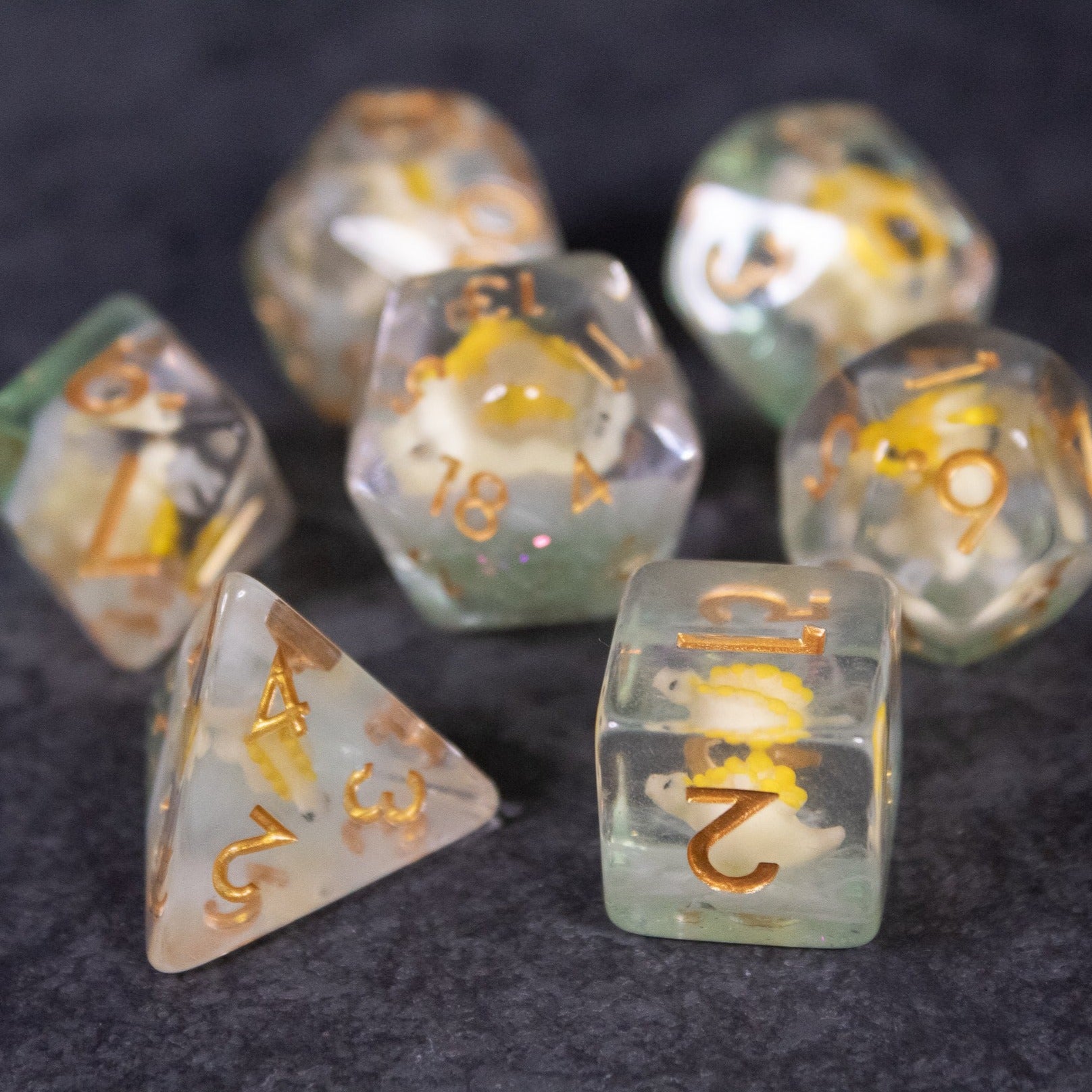 Yellow Stegosaurus Dice Set - Translucent yellow and clear polyhedral dice set with dinosaur scale patterns and gold numbering.
