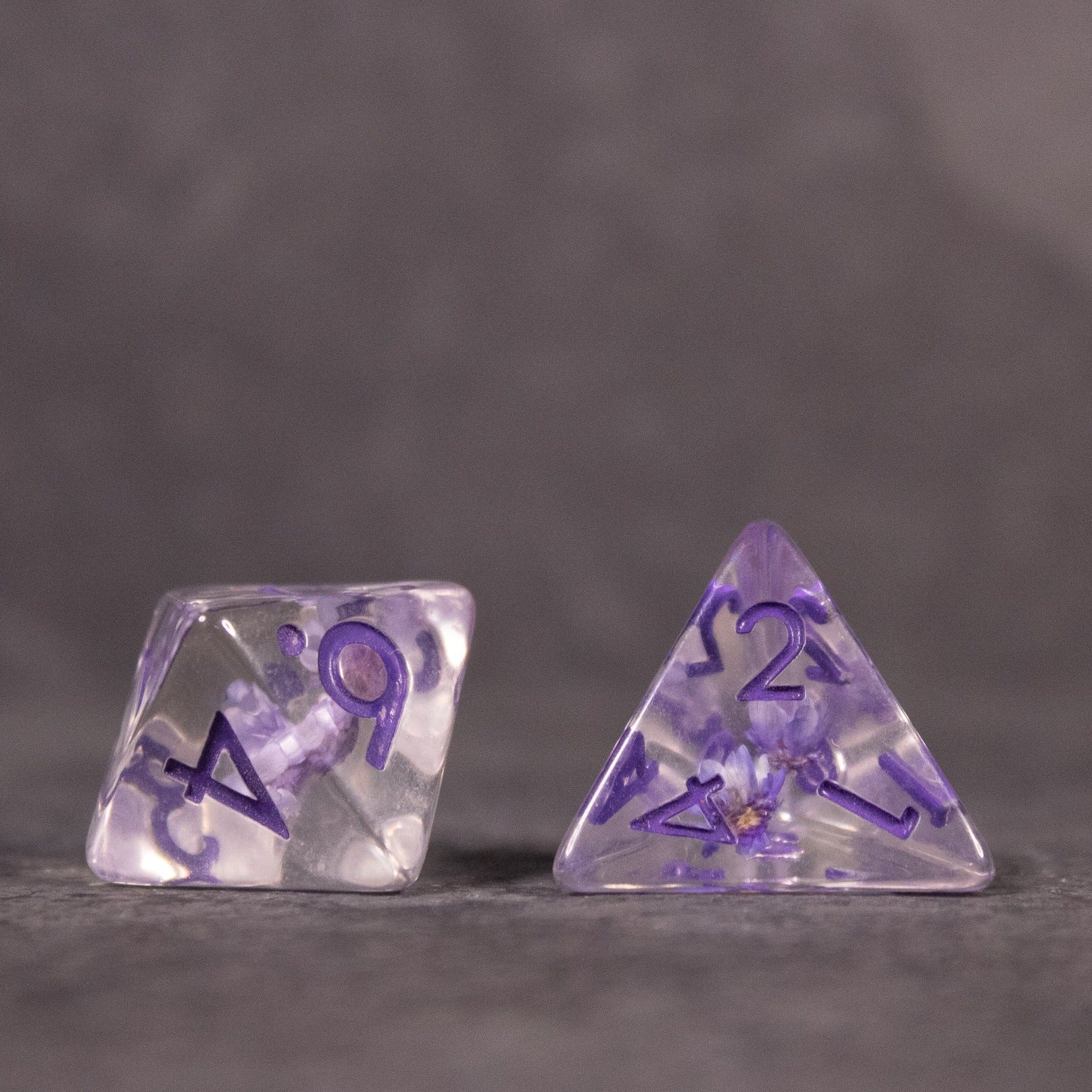 Purple Flower Dice Set - Transparent purple dice with embedded flower designs and purple numbering, including a four-sided and ten-sided die.
