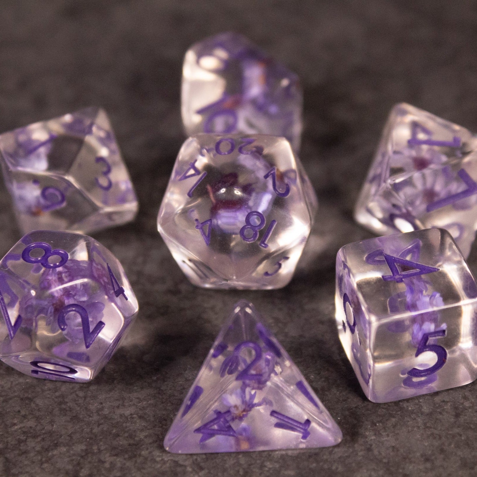 Purple Flower Dice Set - Transparent purple dice set with embedded purple flowers, featuring various polyhedral shapes.
