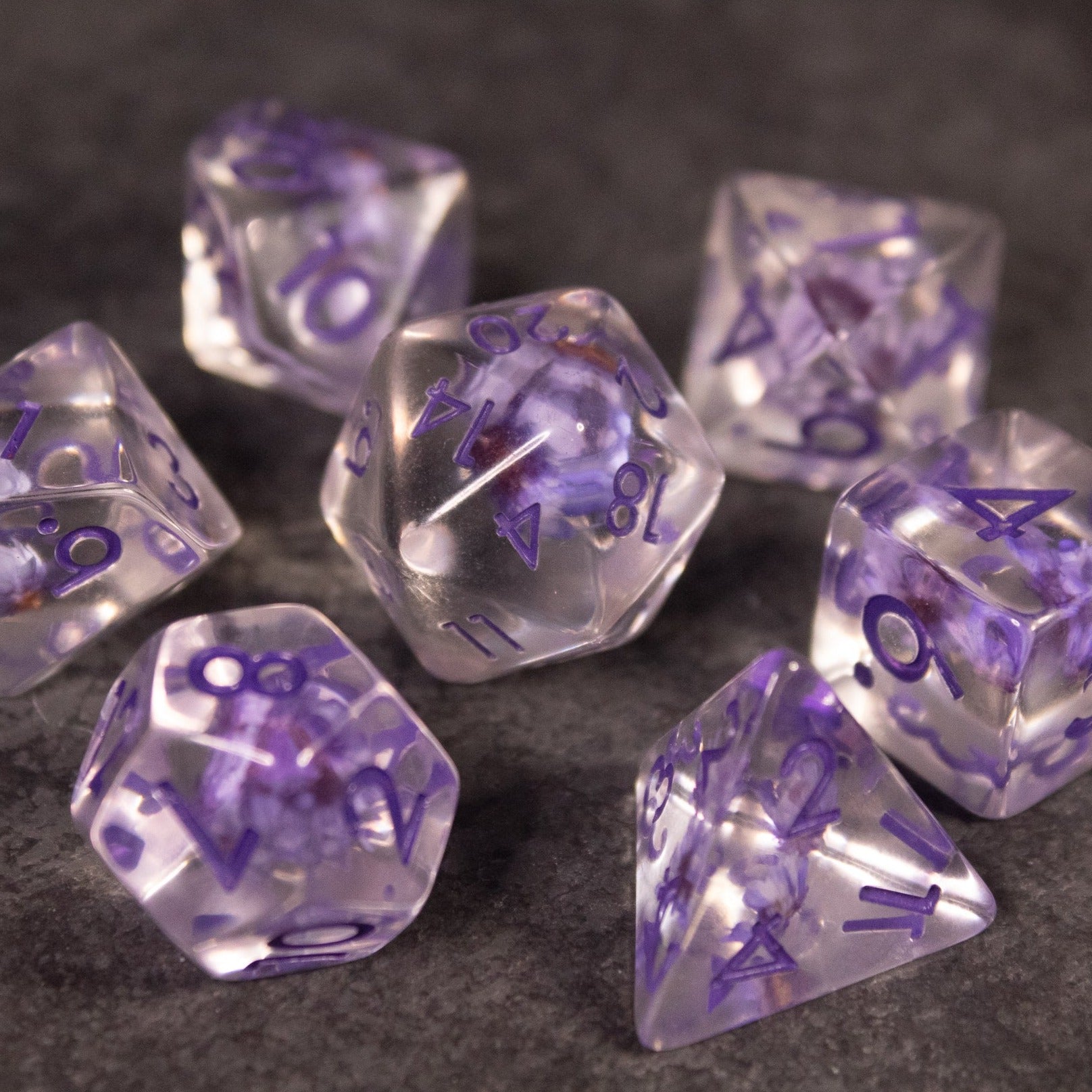 Purple Flower Dice Set - Set of transparent polyhedral dice with purple flower inclusions and purple numbering.