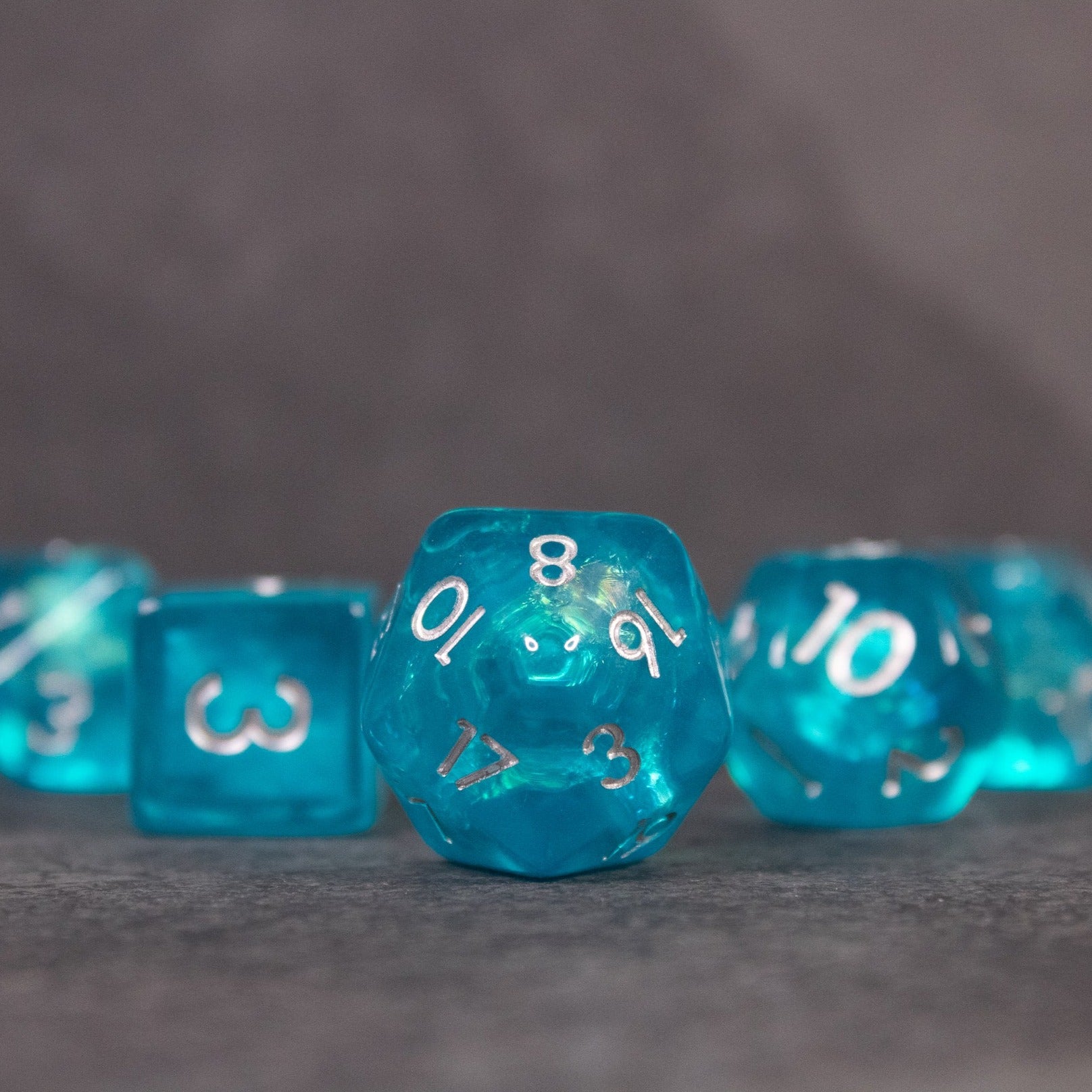 Teal Blue Dice Set - Teal blue iridescent polyhedral dice set with gold numbers, including a d20 and d10.
