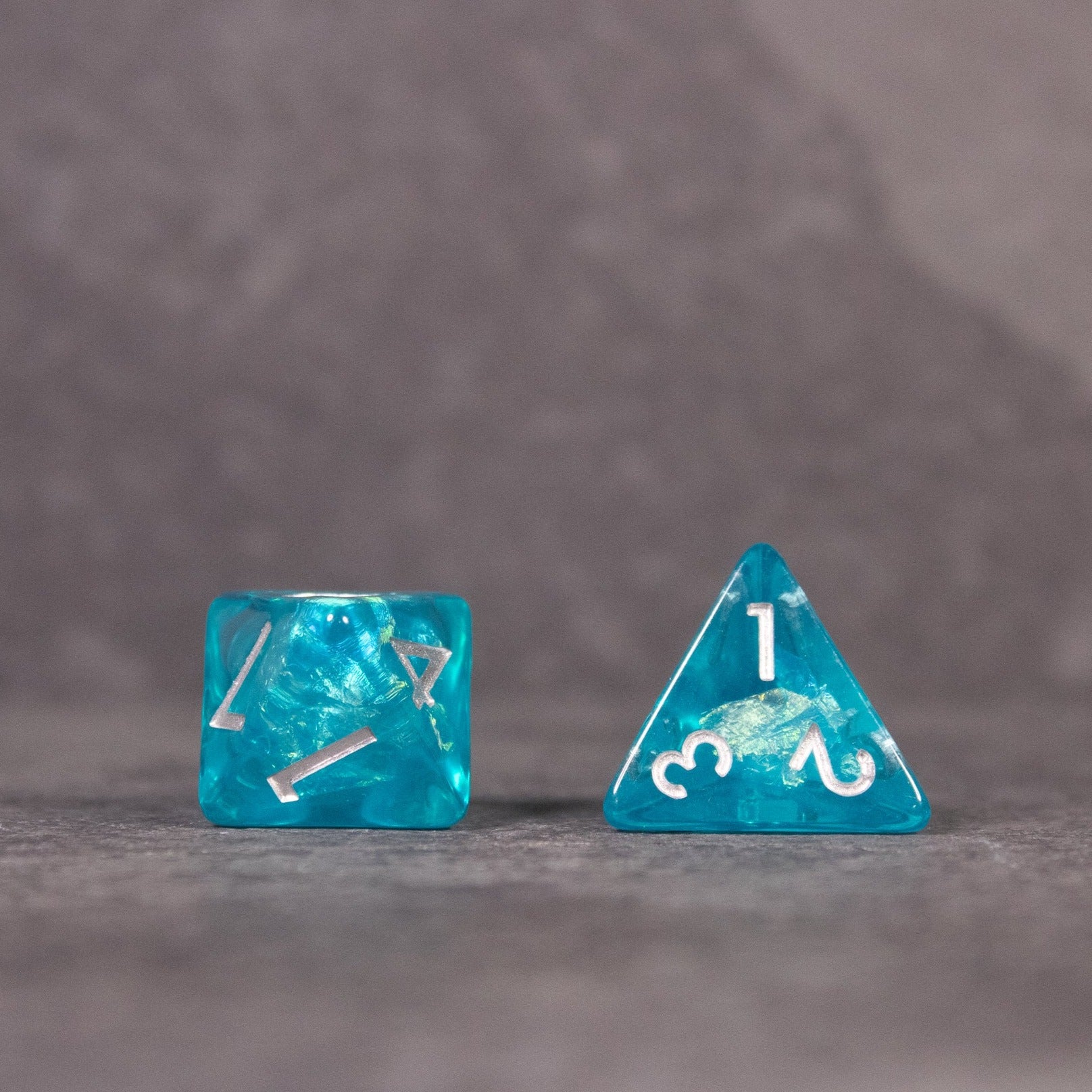 Teal Blue Dice Set - Teal blue iridescent six-sided and four-sided dice with white numbering on a gray surface.