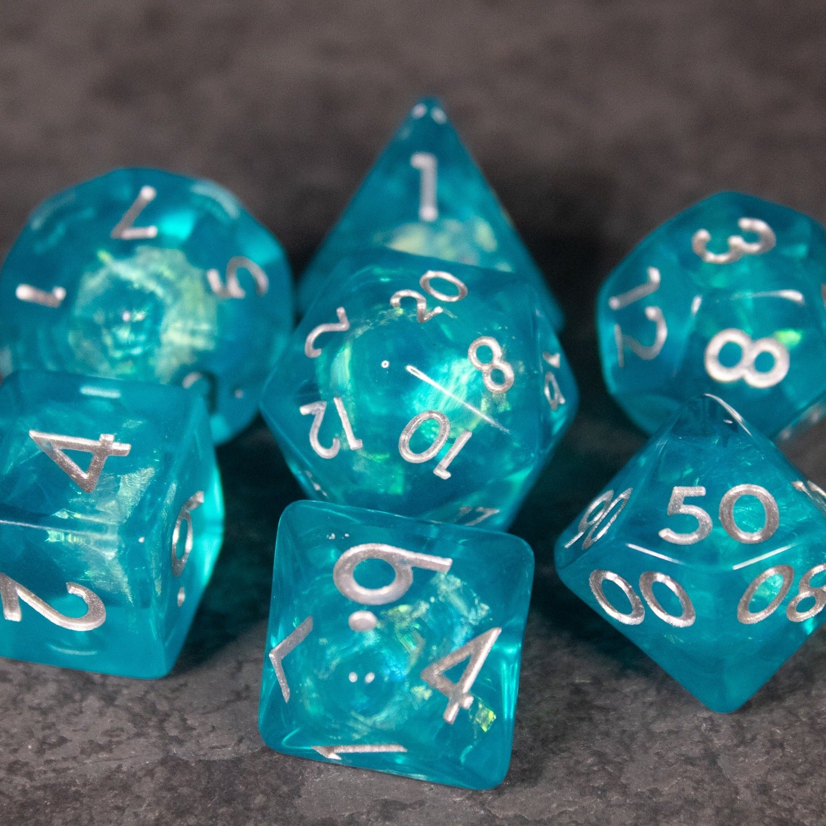 Teal Blue Dice Set - Set of seven iridescent teal blue polyhedral dice with white numbering for tabletop games.