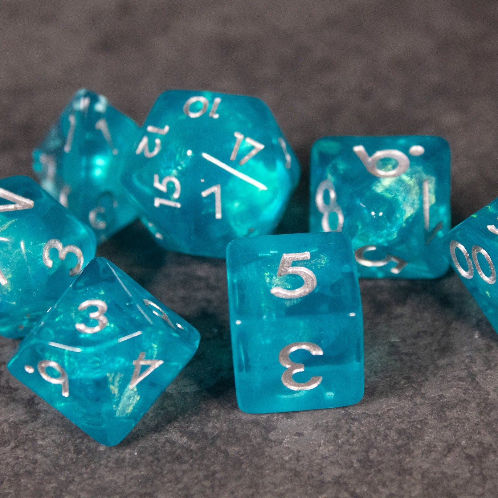 Teal Blue Dice Set - Teal blue iridescent polyhedral dice set with white numbering on gray surface.