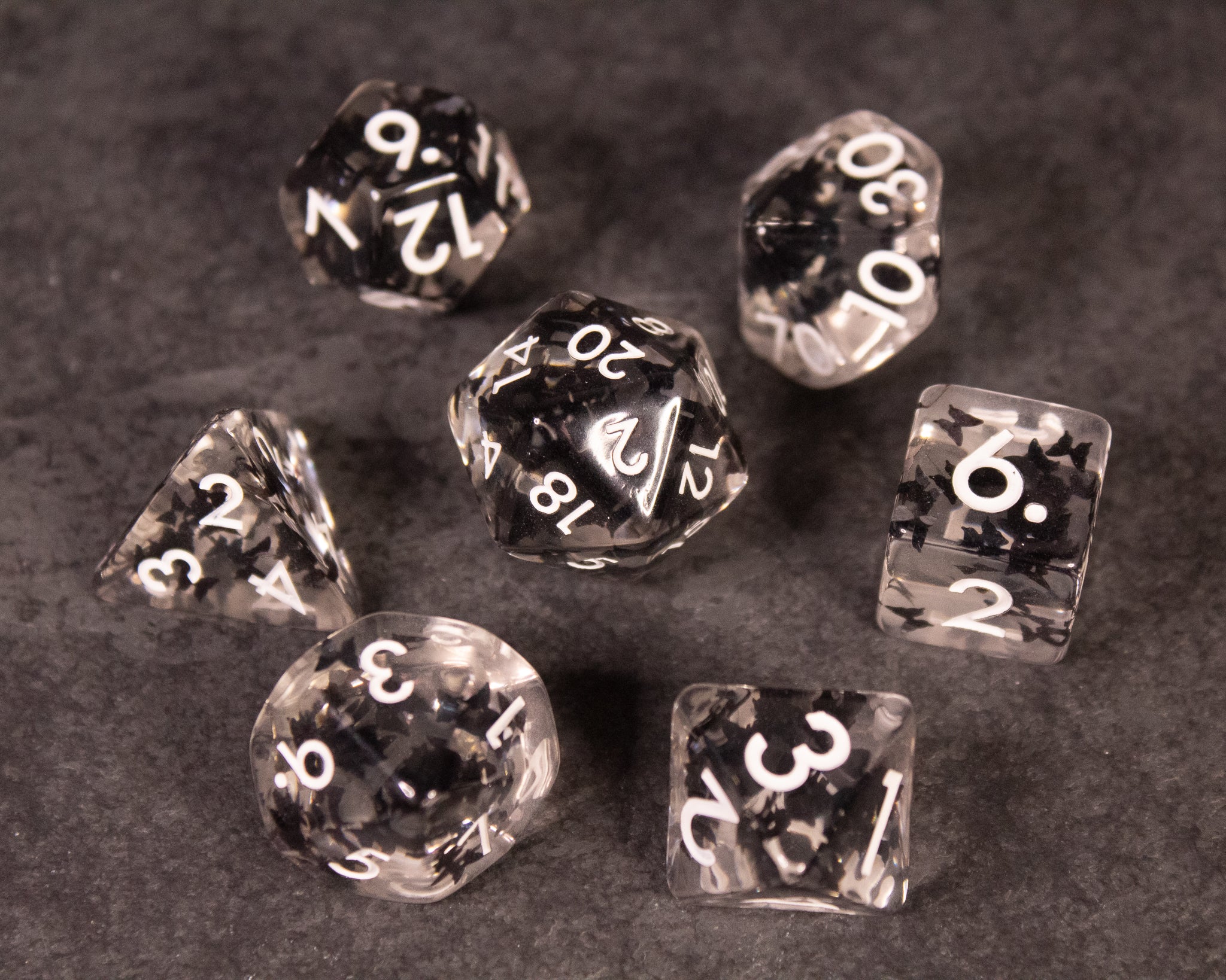 Black Butterfly Dice Set - Set of seven black translucent polyhedral dice with white numbers and subtle butterfly designs inside.