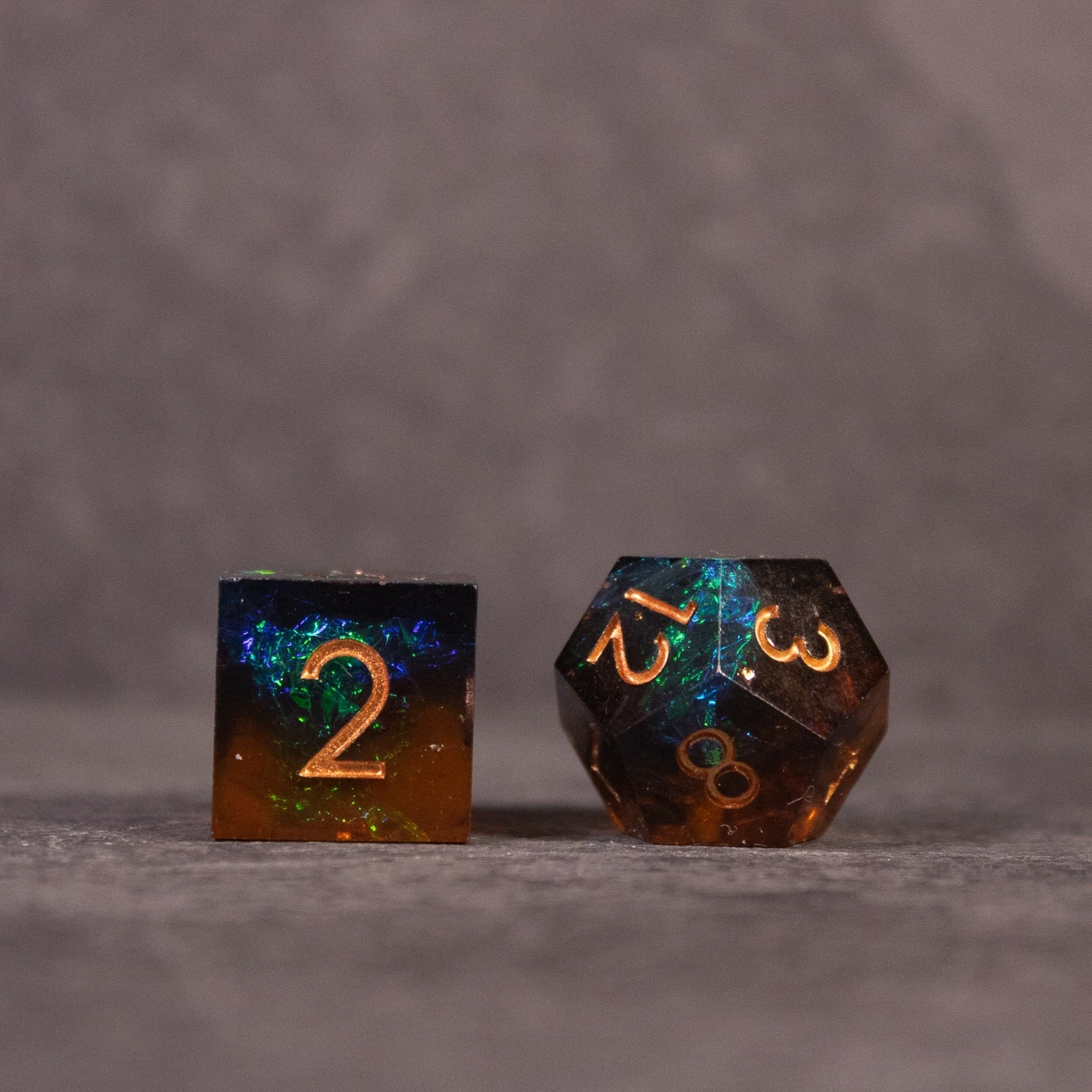 Whiskeyjack Dice Set - Two translucent polyhedral dice with sharp edges in blue and amber tones, featuring gold numbering.