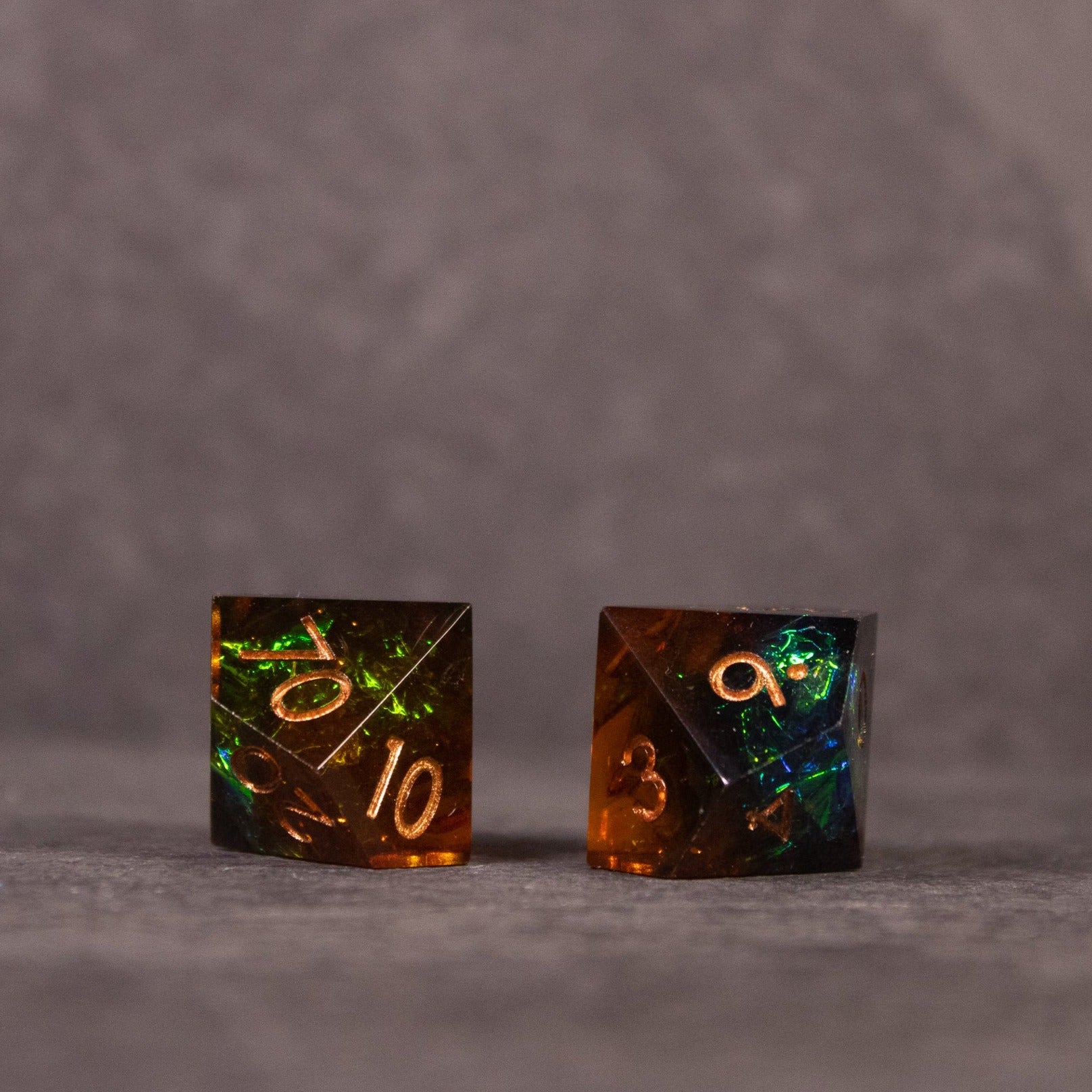 Whiskeyjack Dice Set - Two dark translucent sharp-edged dice with glowing orange and green numbers and internal flecks.