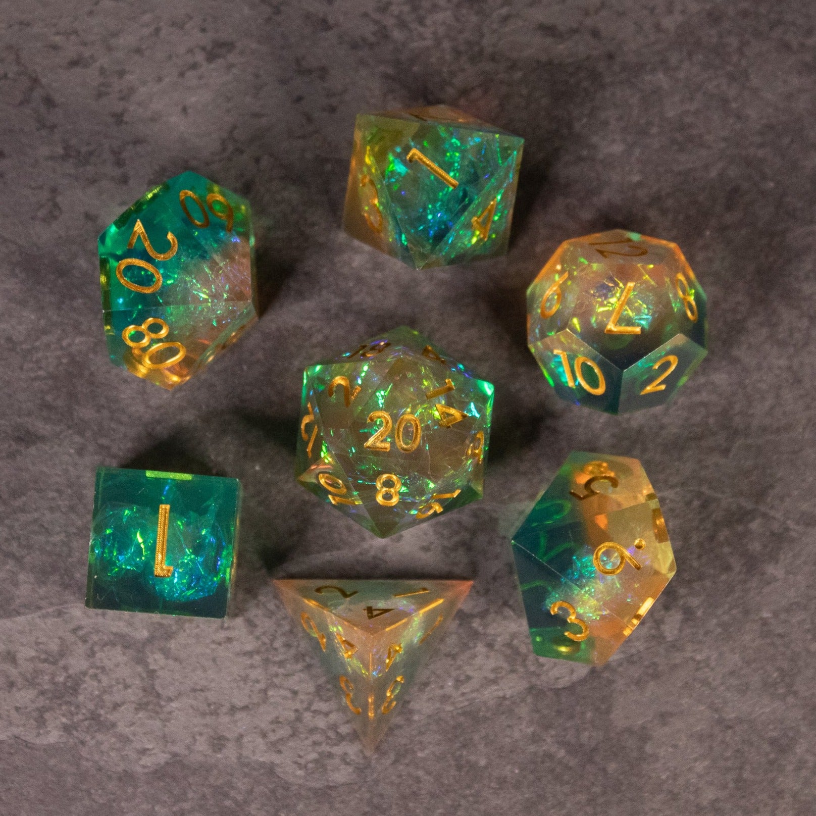 Seafarer Dice Set - Seven green and orange translucent sharp-edged polyhedral dice with gold numbering on a gray surface.