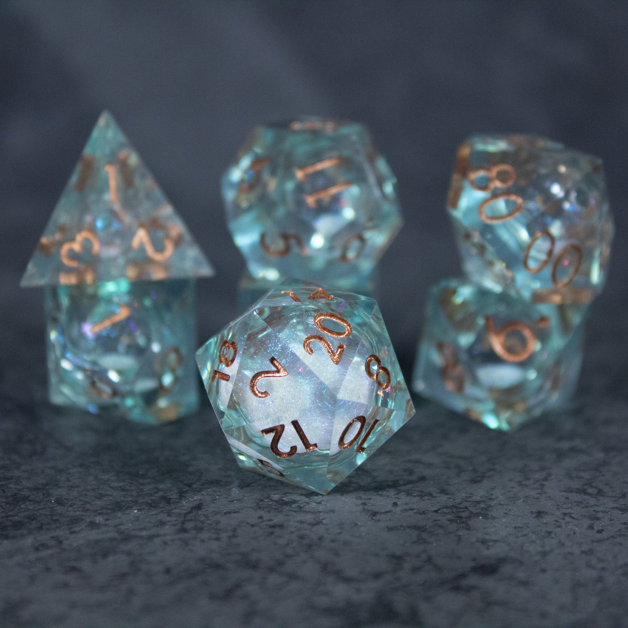 Will o' Wisp Liquid Core Dice Set - Set of translucent blue-green sharp-edged polyhedral dice with copper numbers, containing swirling liquid cores.